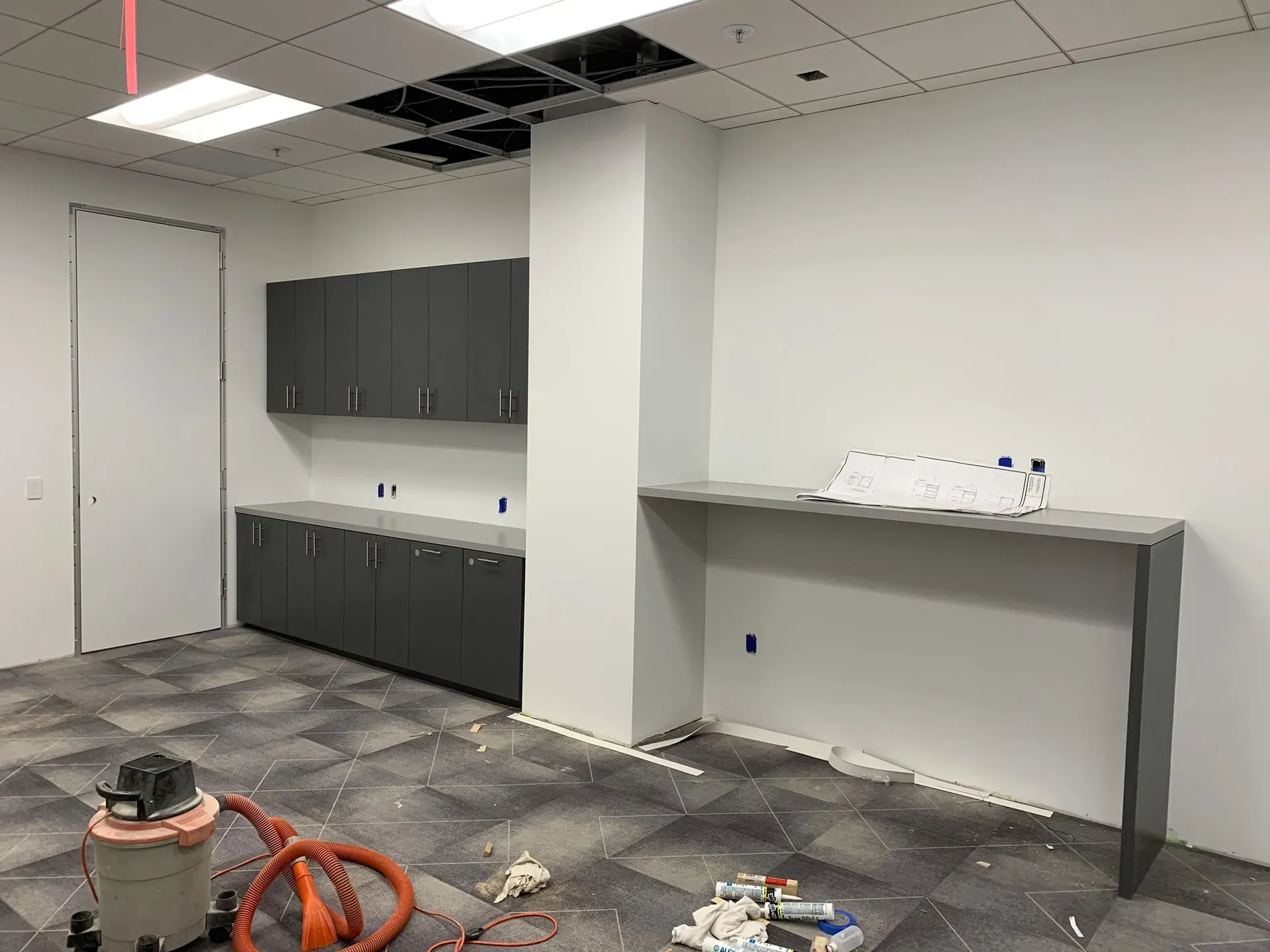 Partially finished office room with cabinets, a long table, and construction debris on the floor