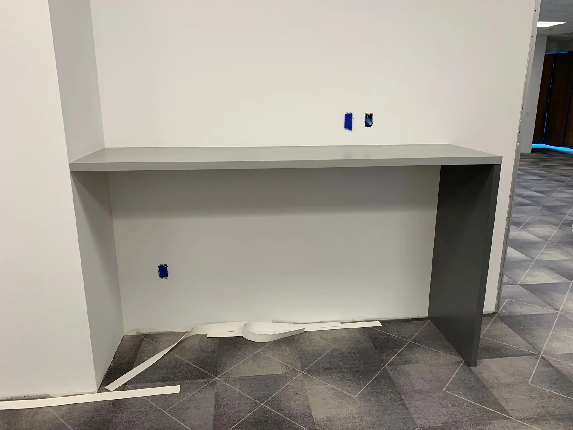Built-in desk nook with white shelves, gray side panel, and tiled floor in an empty room