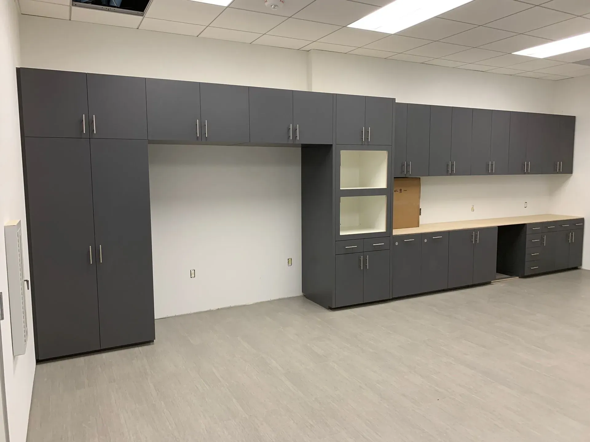 Gray wall-to-wall cabinets in a vacant office or storage room with a large open center alcove and beige floor