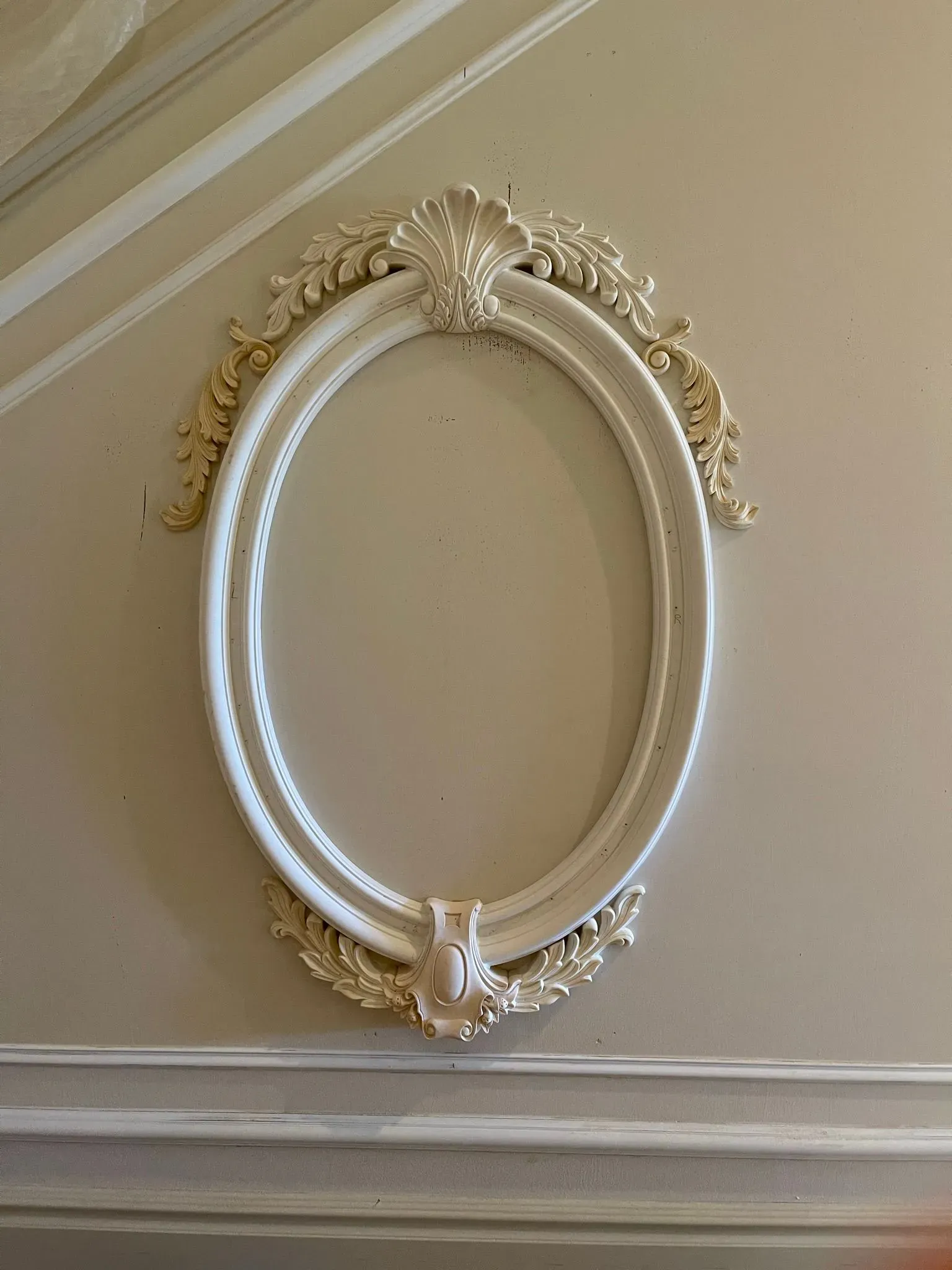 Ornate oval white and gold wall frame on a cream paneled wall