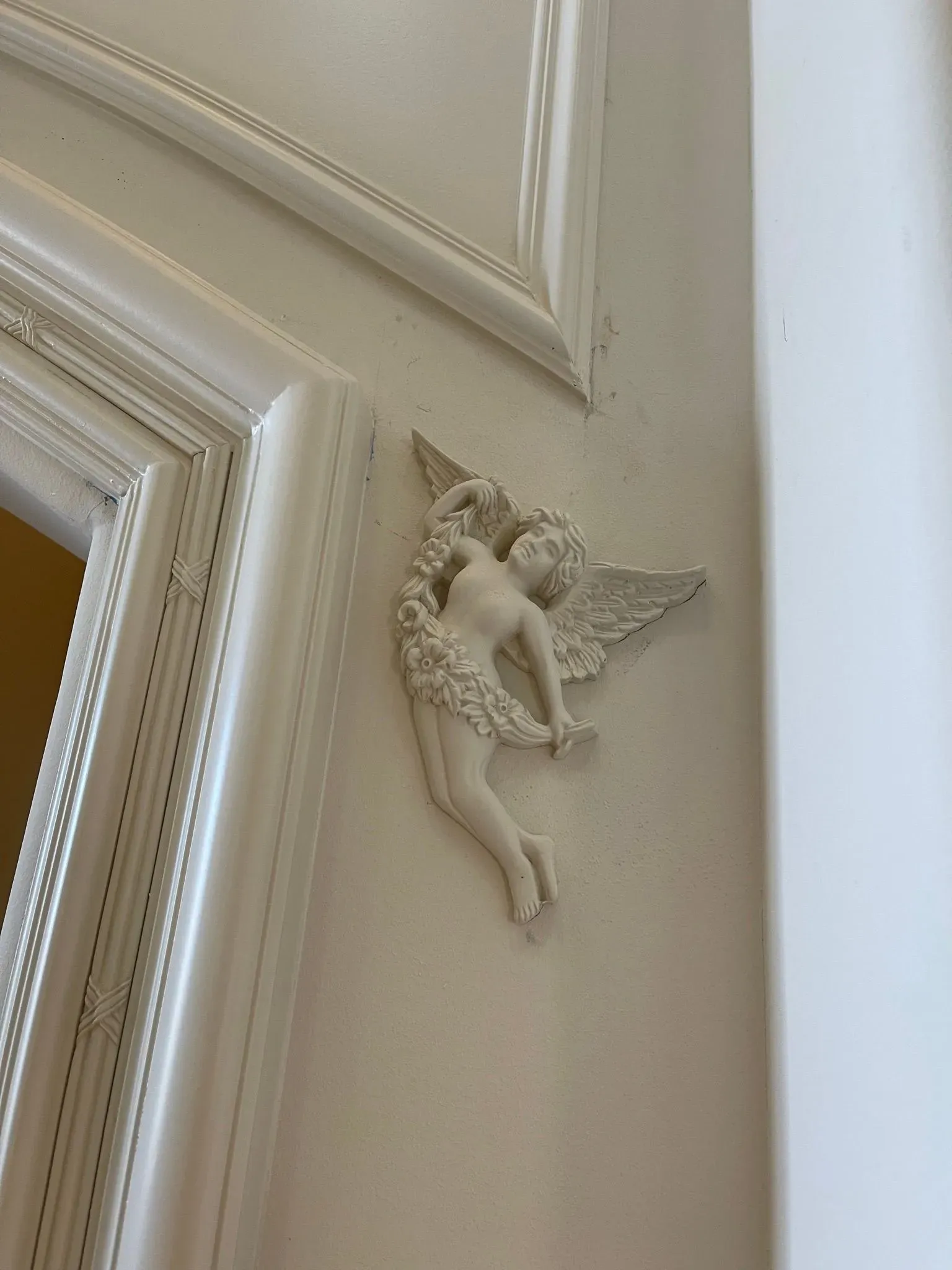 Small angel figurine mounted on a cream-colored wall beside a framed molding detail