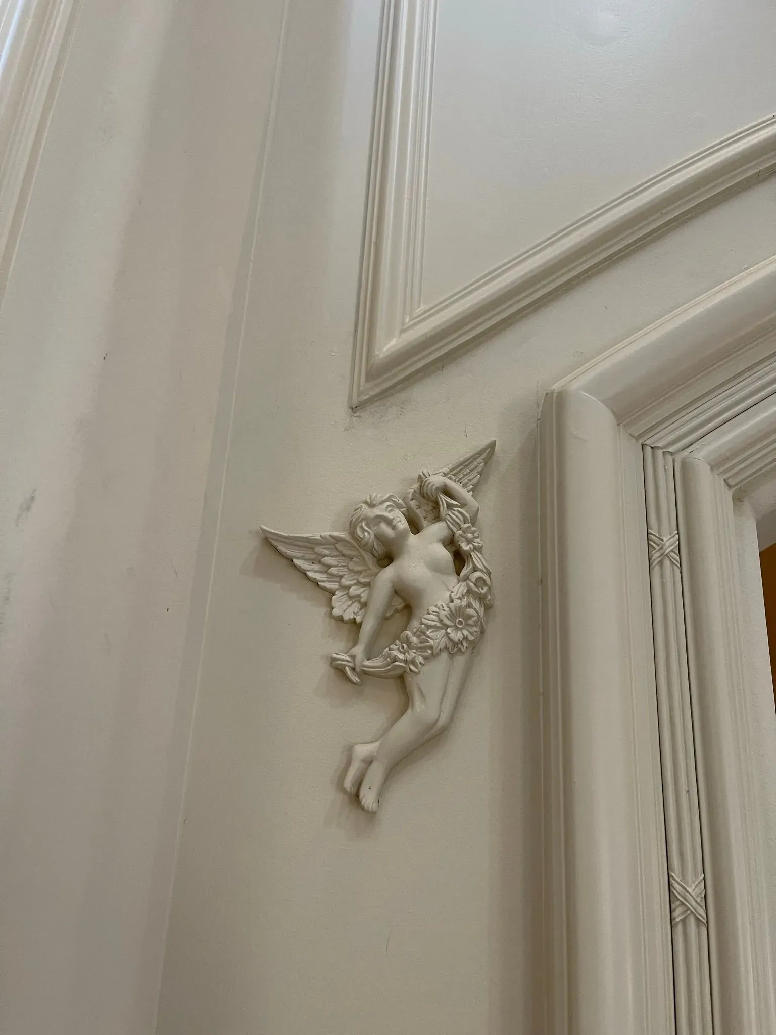 Small white angel wall ornament on a cream interior wall near a doorway.