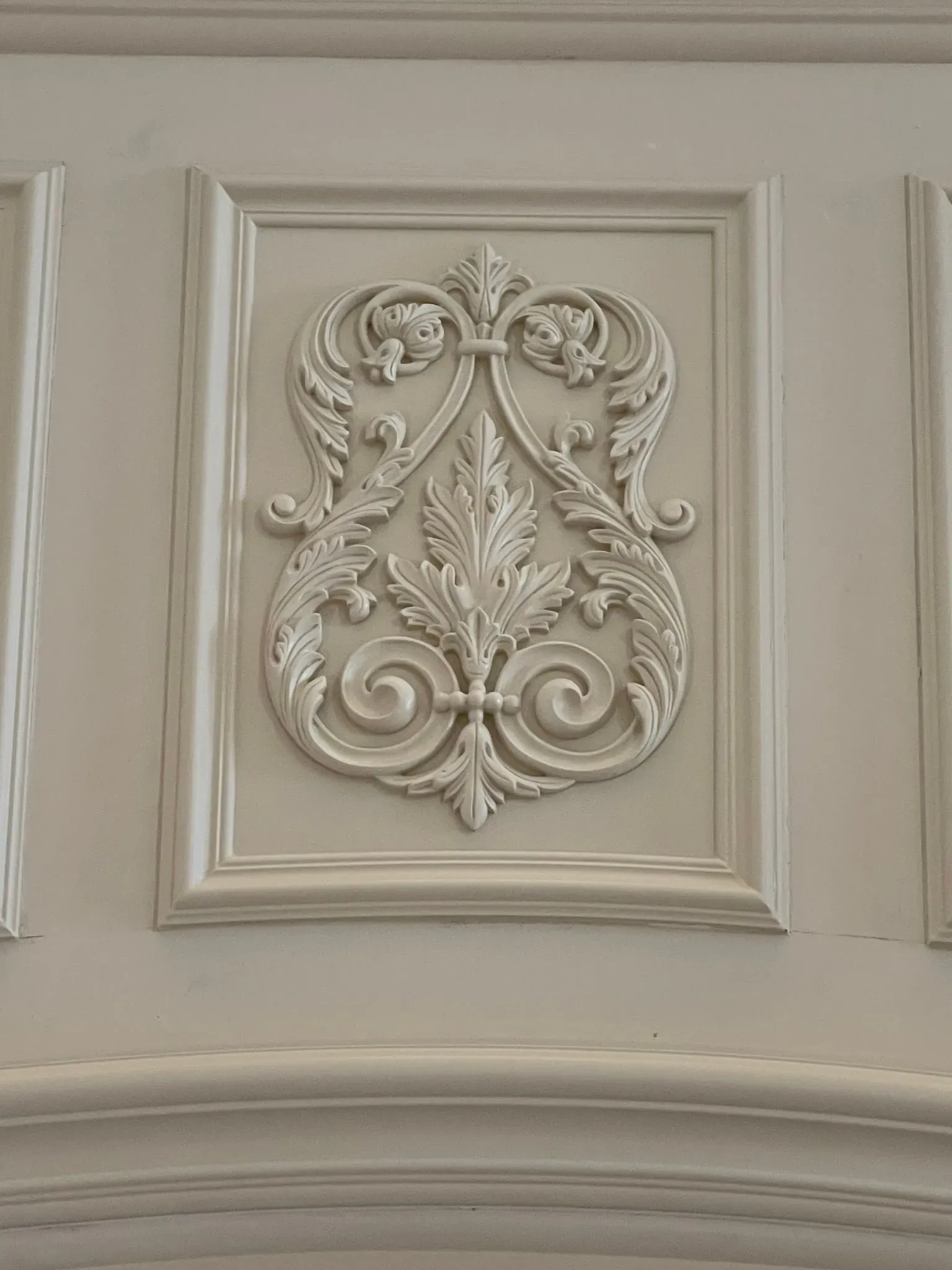 Decorative cream-colored carved floral panel on a paneled wall