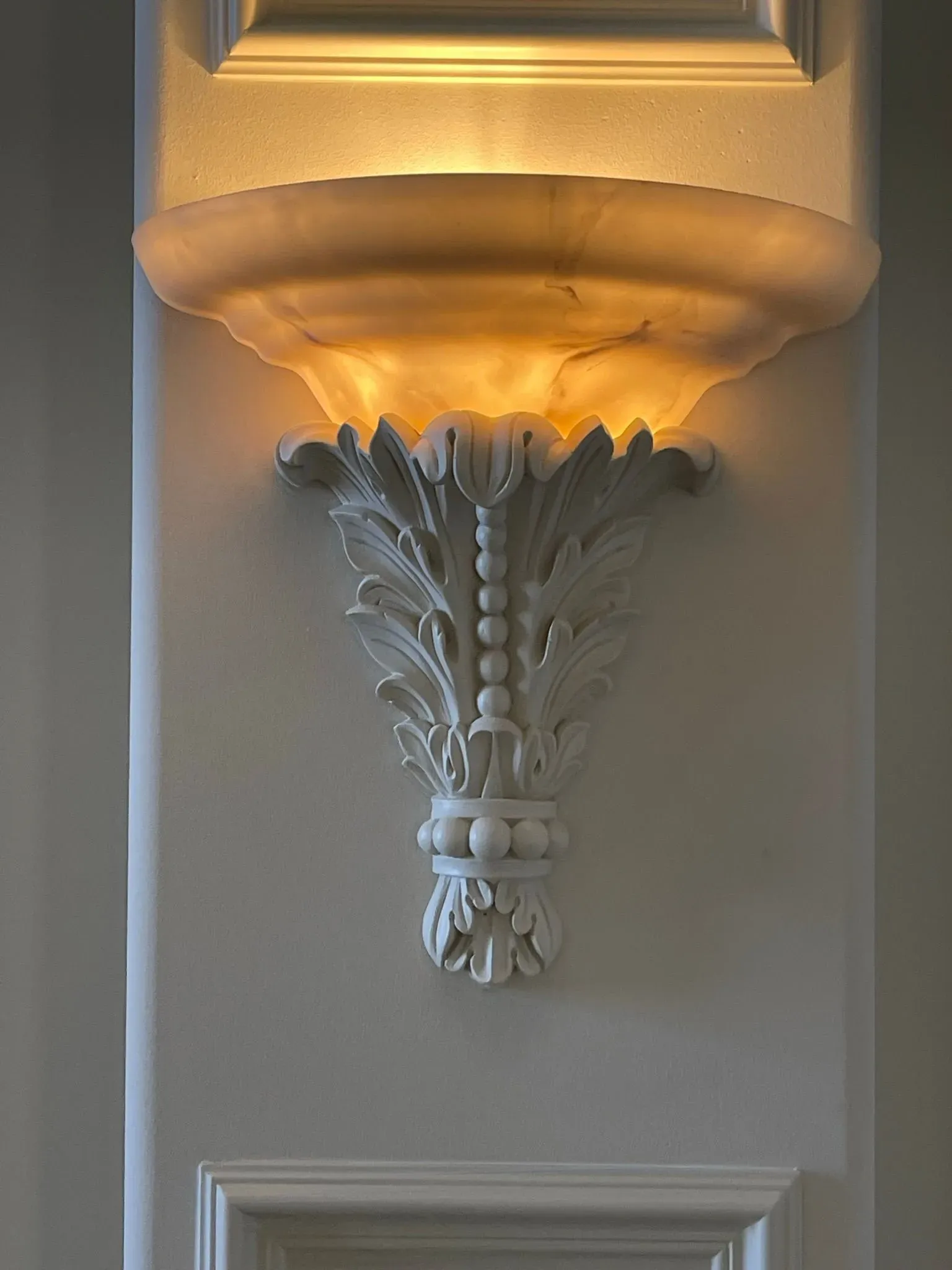 Decorative white wall sconce with warm amber light on a paneled wall