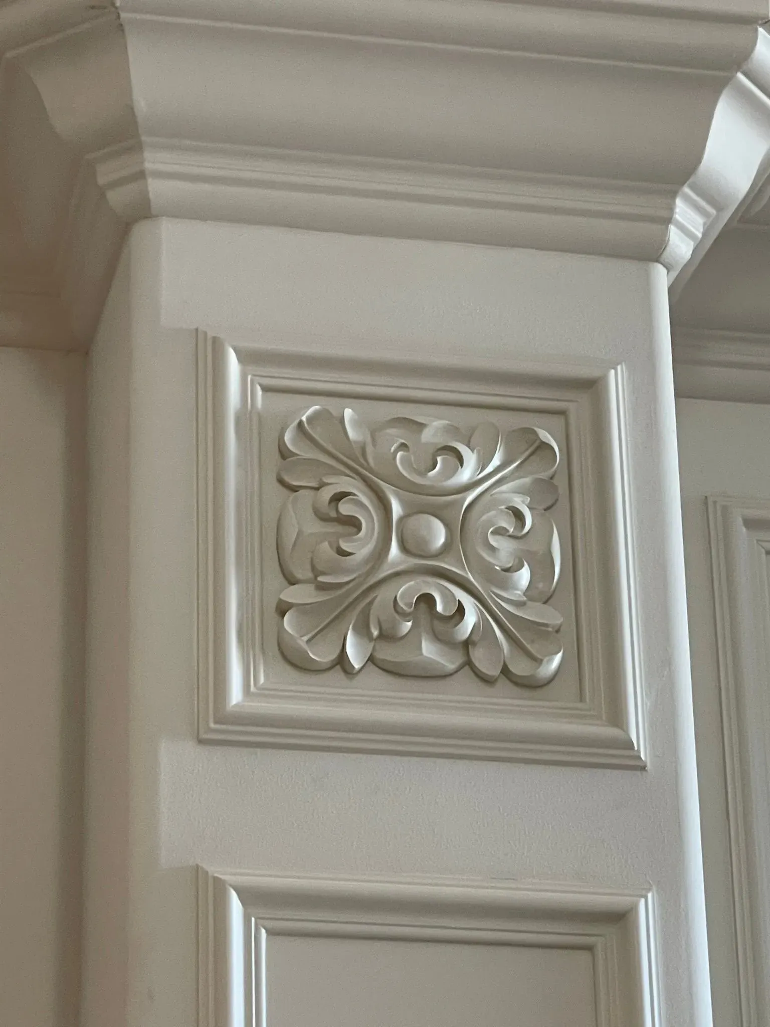 Decorative white carved trim on a building column with a floral square panel