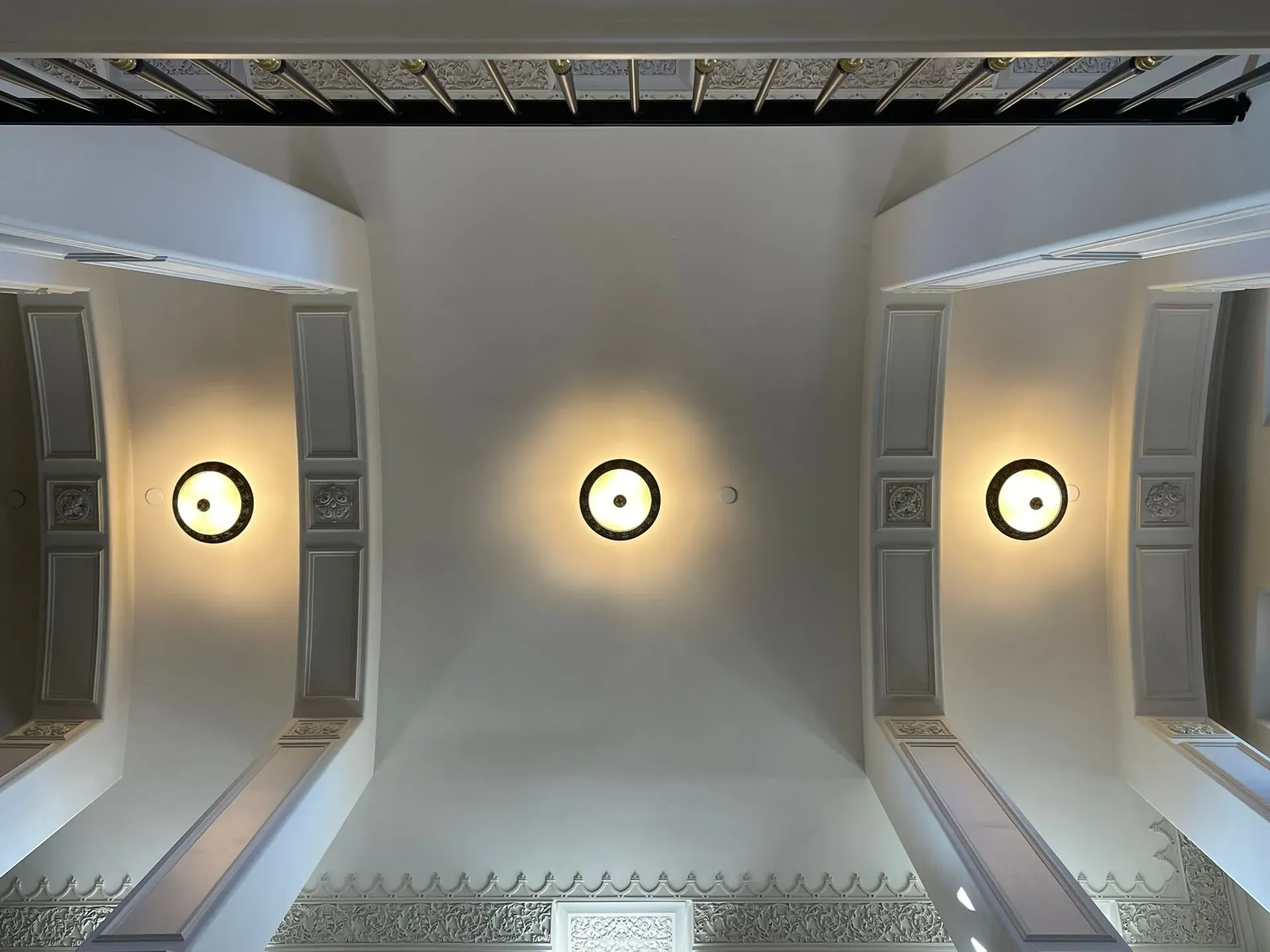 Ceiling view of three round lights in a white room with architectural molding and skylights