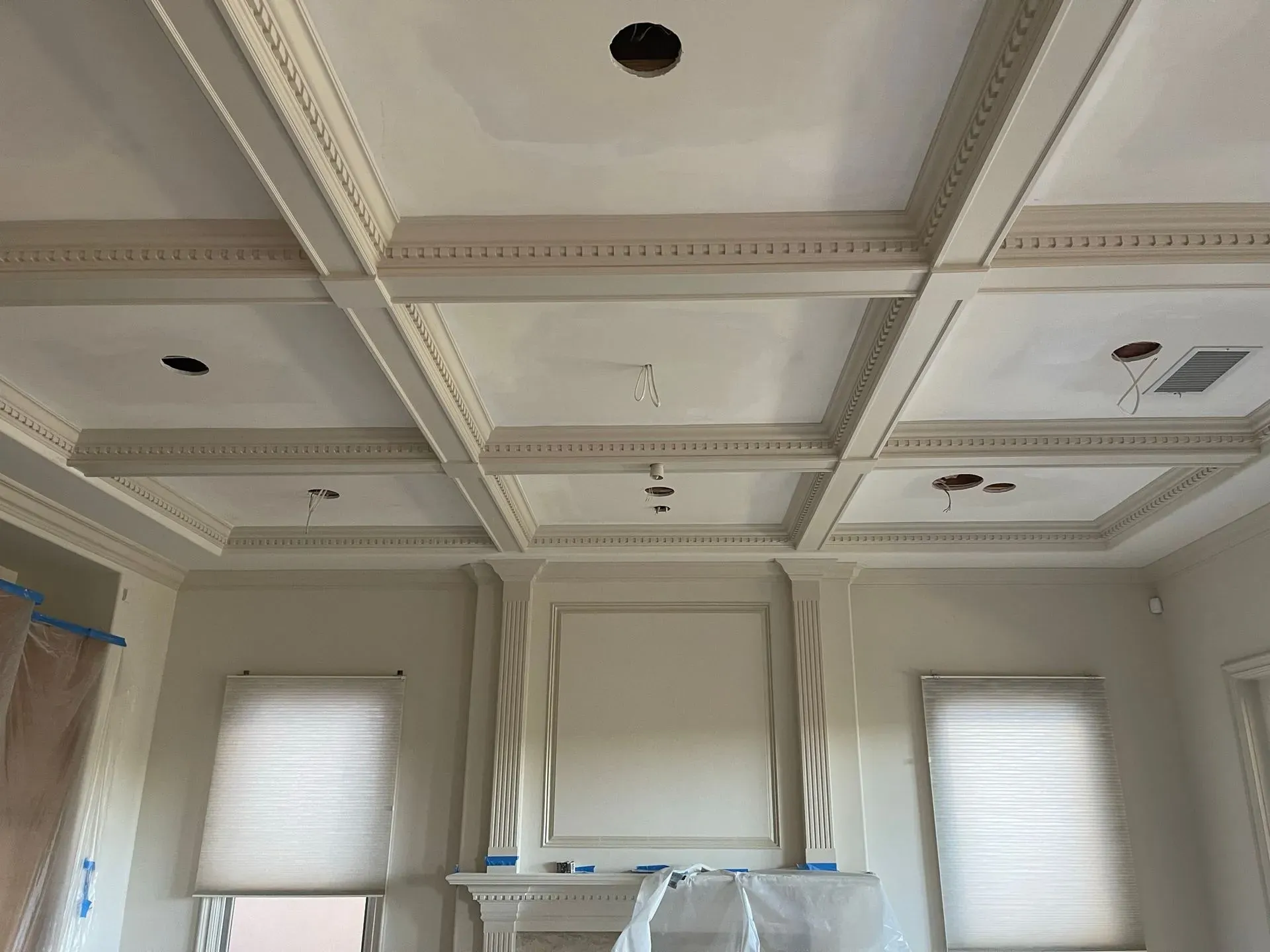 White coffered ceiling with recessed lights above a kitchen wall and two windows with blinds