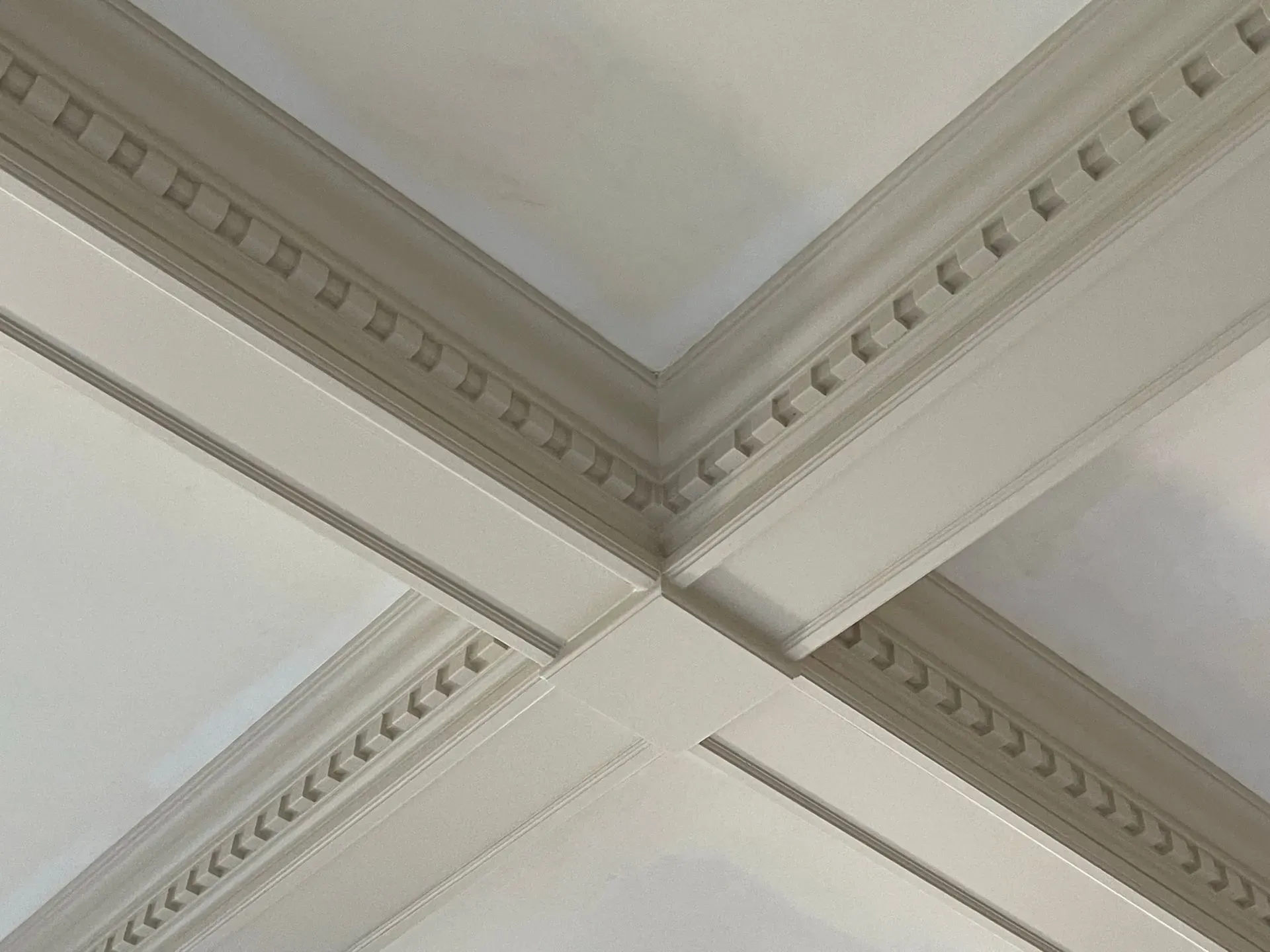 White ceiling corner with decorative crown molding and intersecting beams