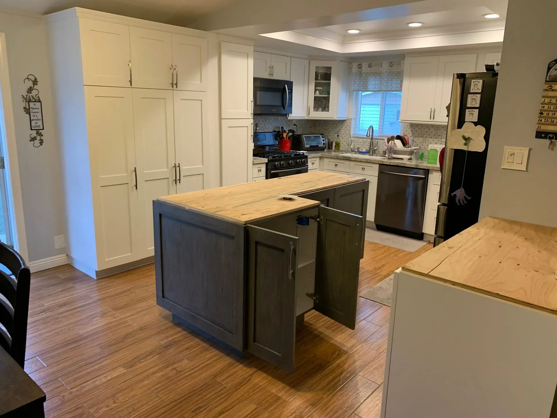 Bright kitchen with white cabinets, dark island, and wood floors; open doorway to adjacent room.
