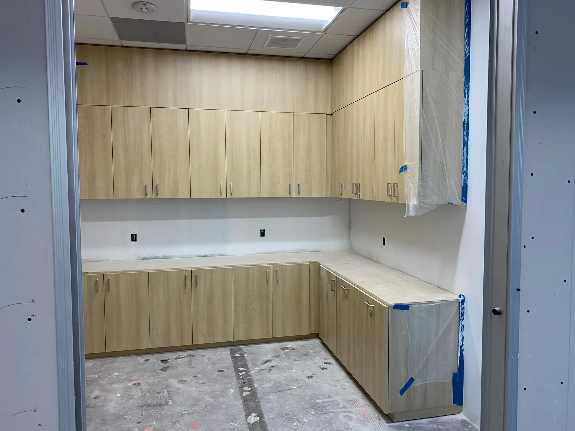 Unfinished kitchen with wood cabinets, white countertops, and bare concrete floor in a small room