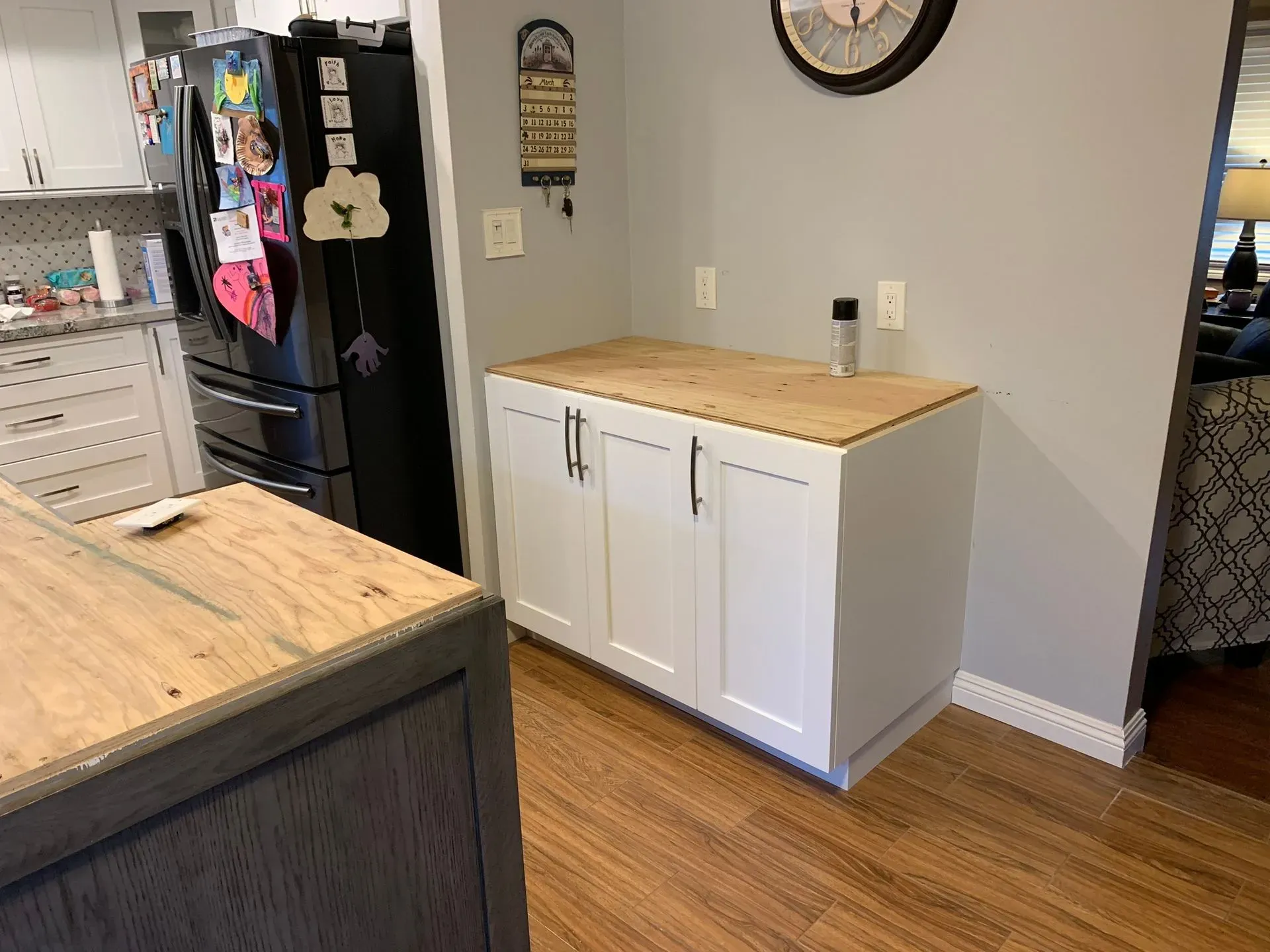 Kitchen with white cabinets and wood countertops, black refrigerator, and hardwood floor.