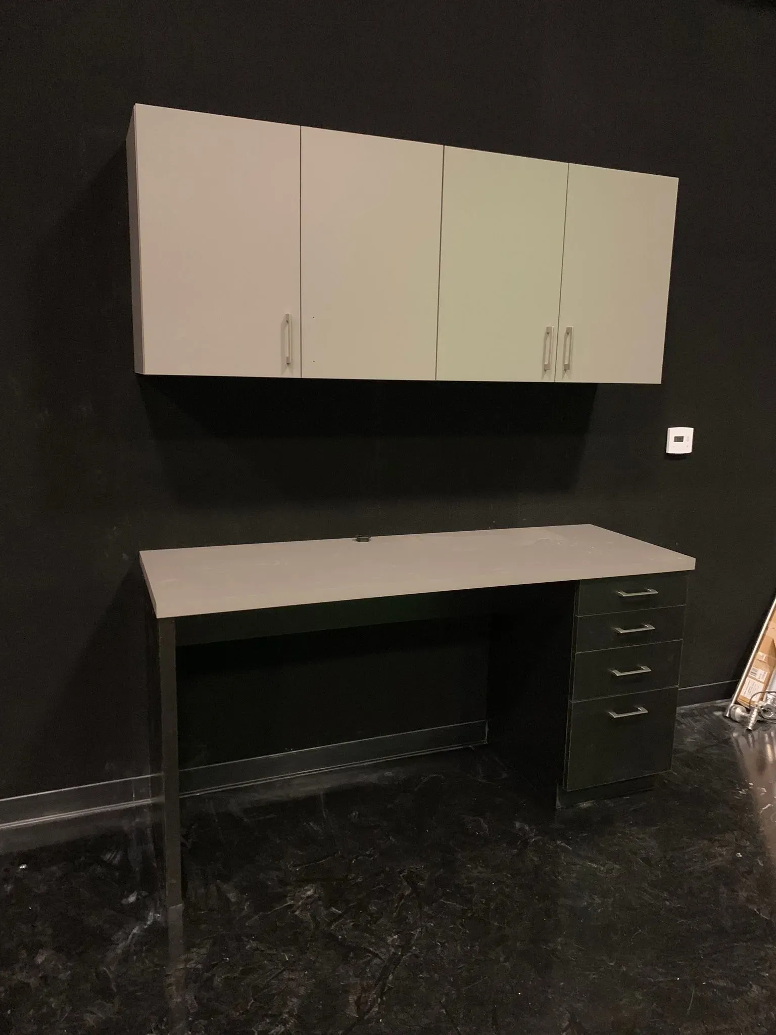 Black wall-mounted cabinets above a workbench in a dark room with a black floor.