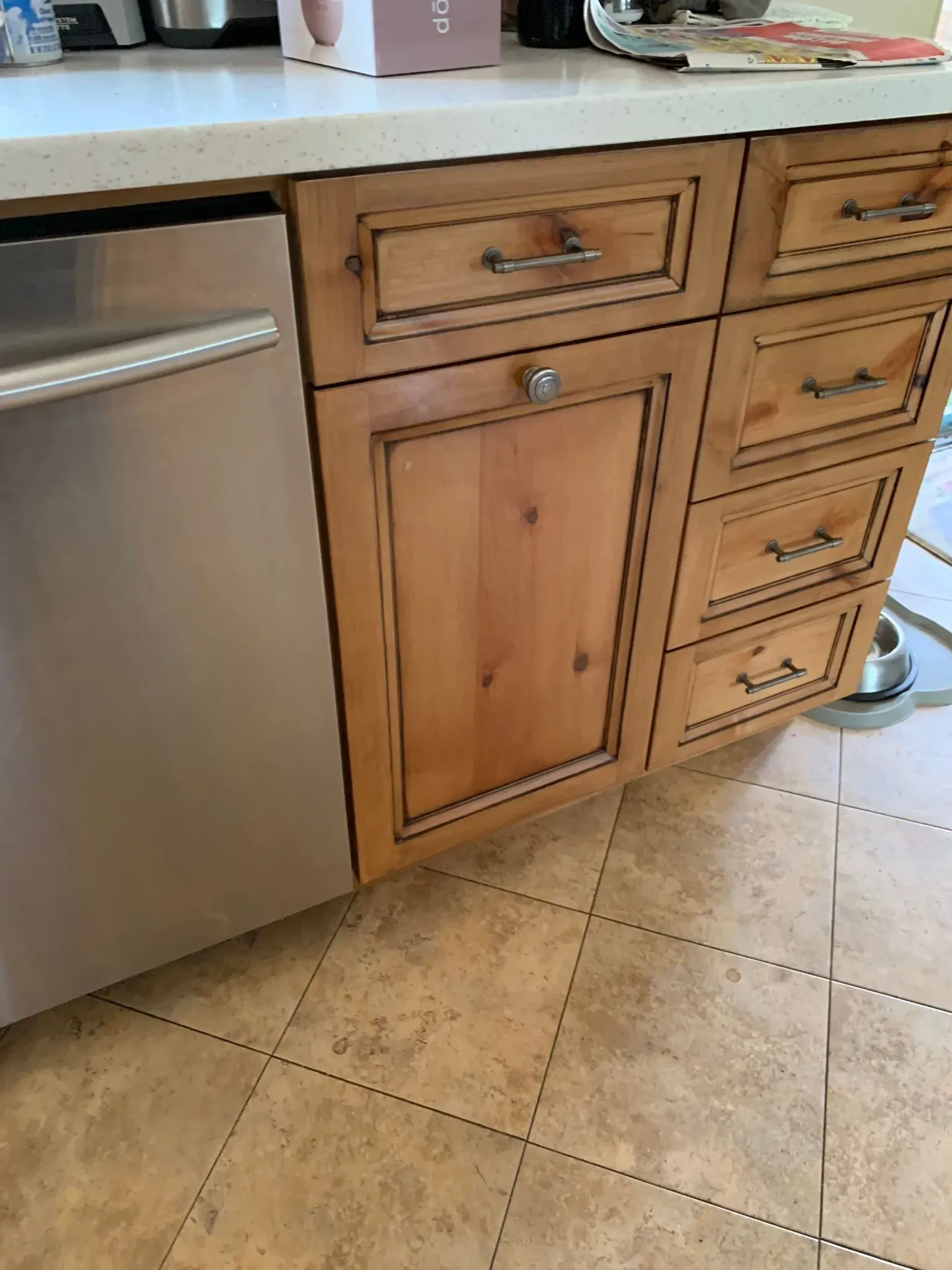 Kitchen cabinets beside a stainless steel dishwasher and tiled floor