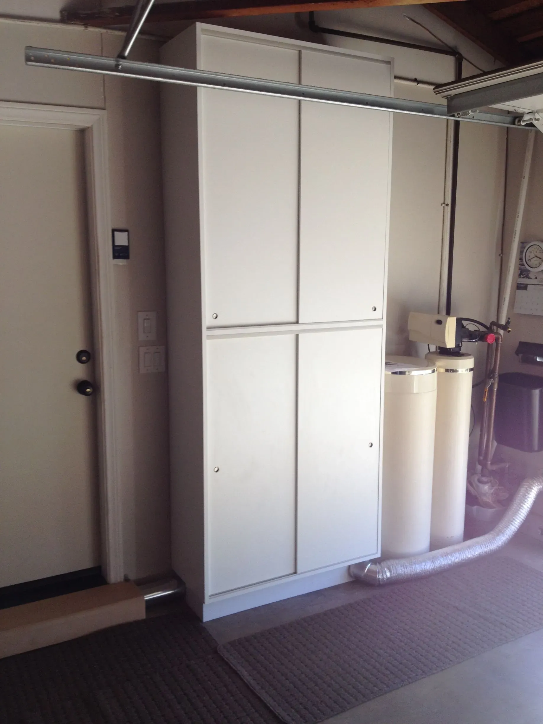 White storage cabinets and a water heater in a utility room with exposed pipes and carpeted floor