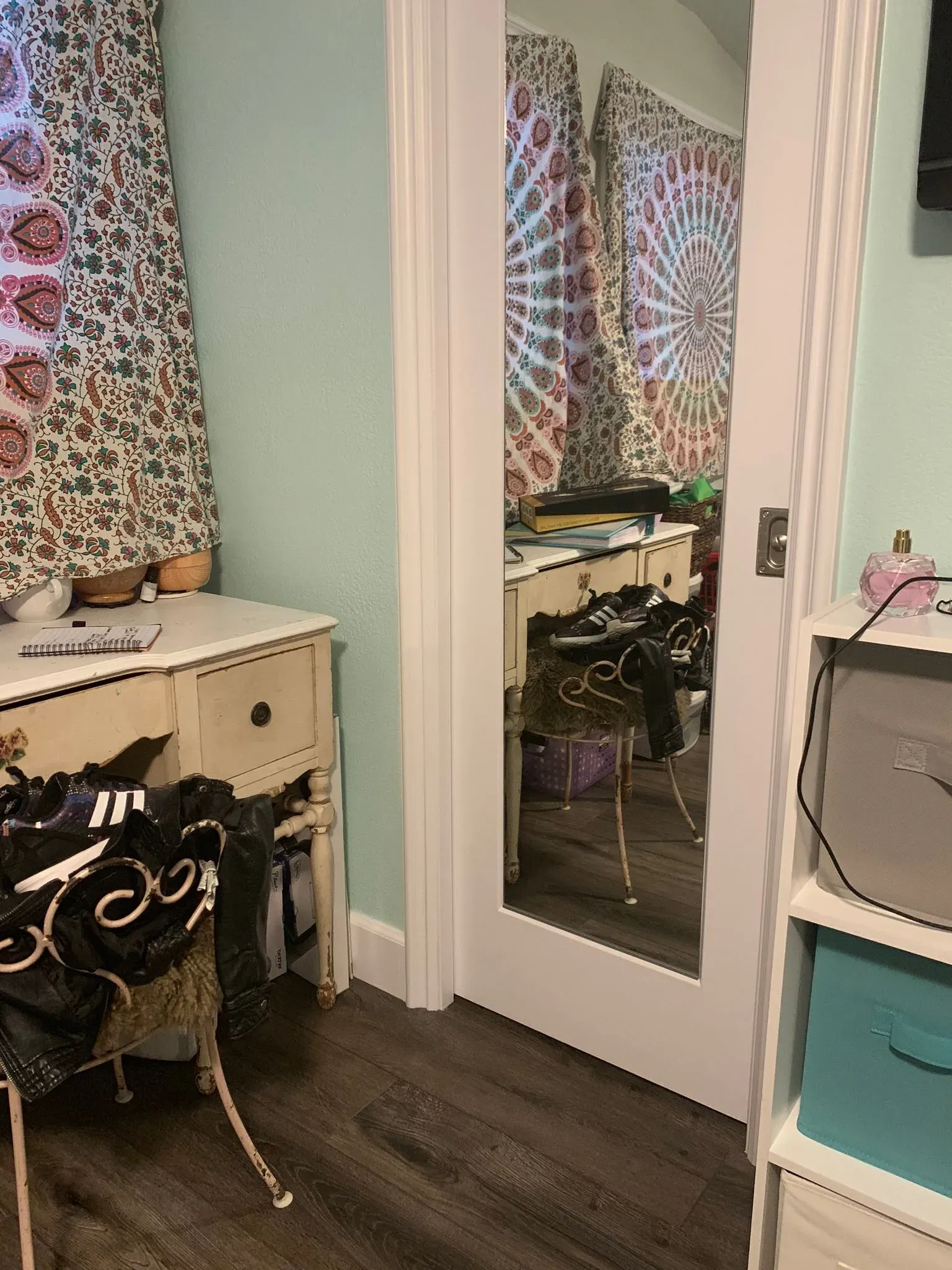 Bedroom vanity with mirror, desk, chair, and patterned curtains in a mint-green room.