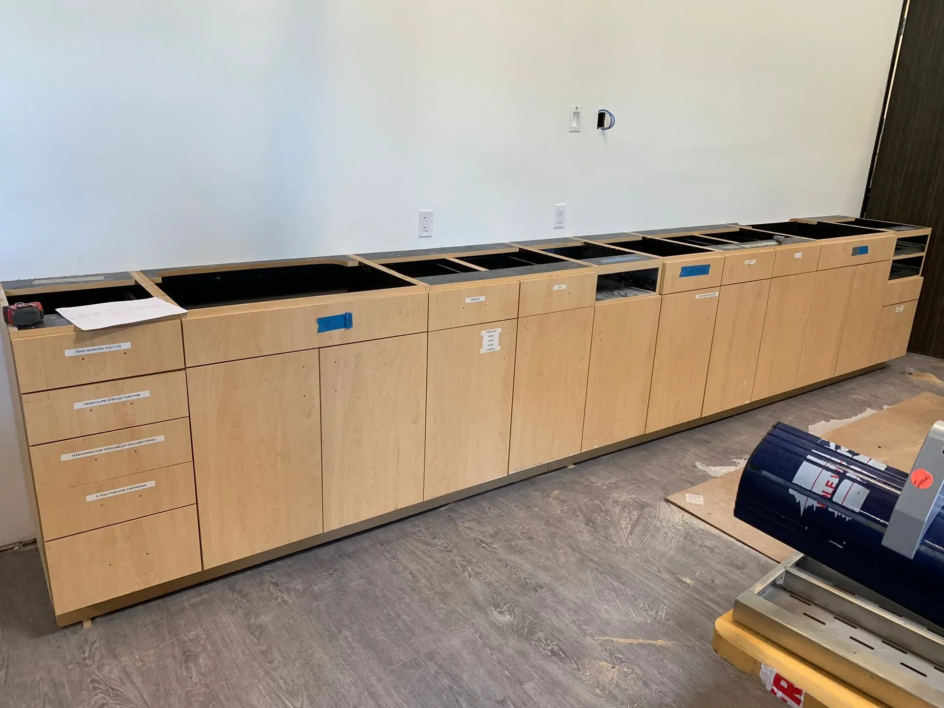 Long row of unfinished wooden office cabinets and countertop against a blank wall.