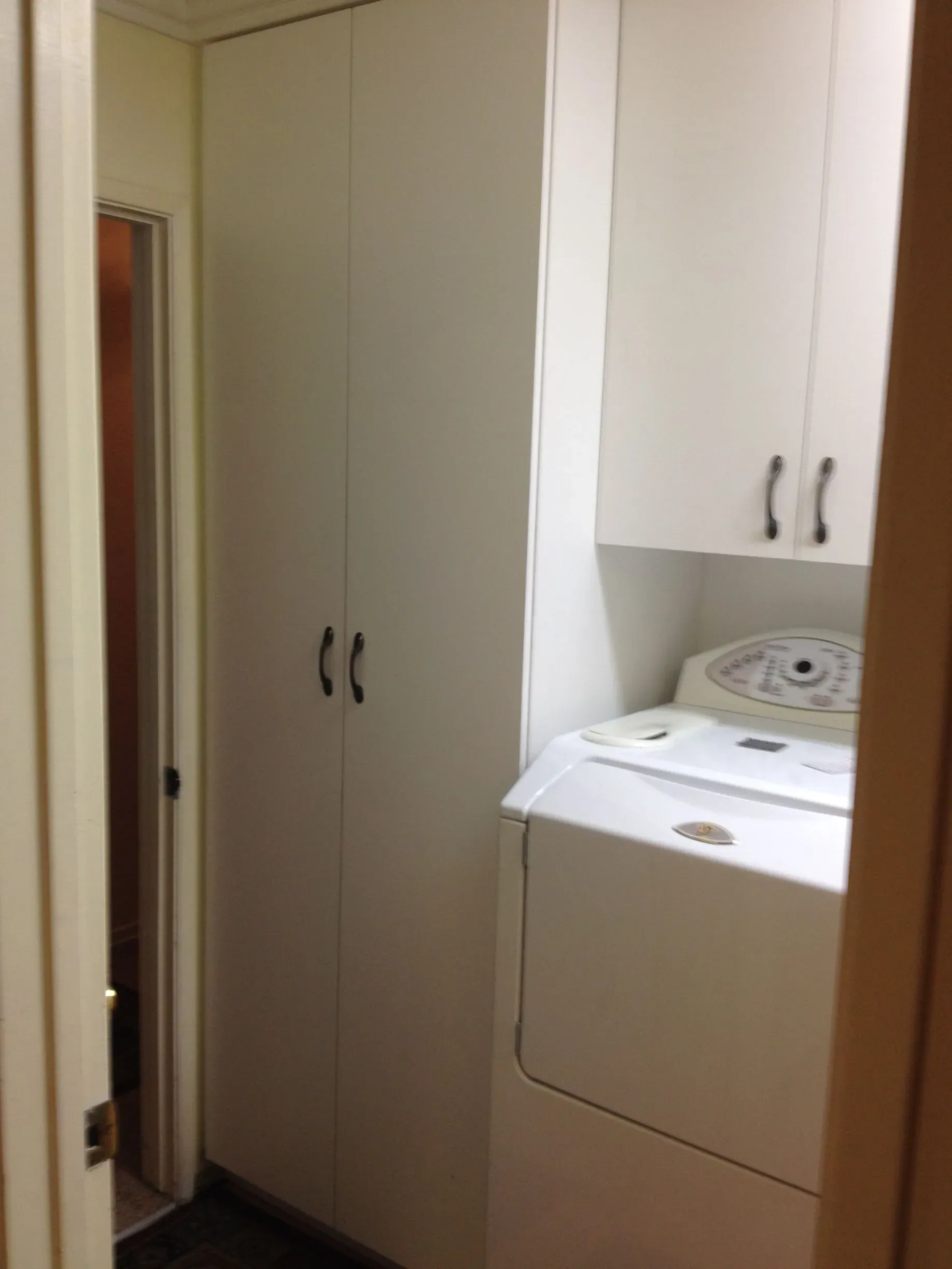 Small laundry nook with stacked washer and dryer beside tall beige cabinets in a narrow hallway.