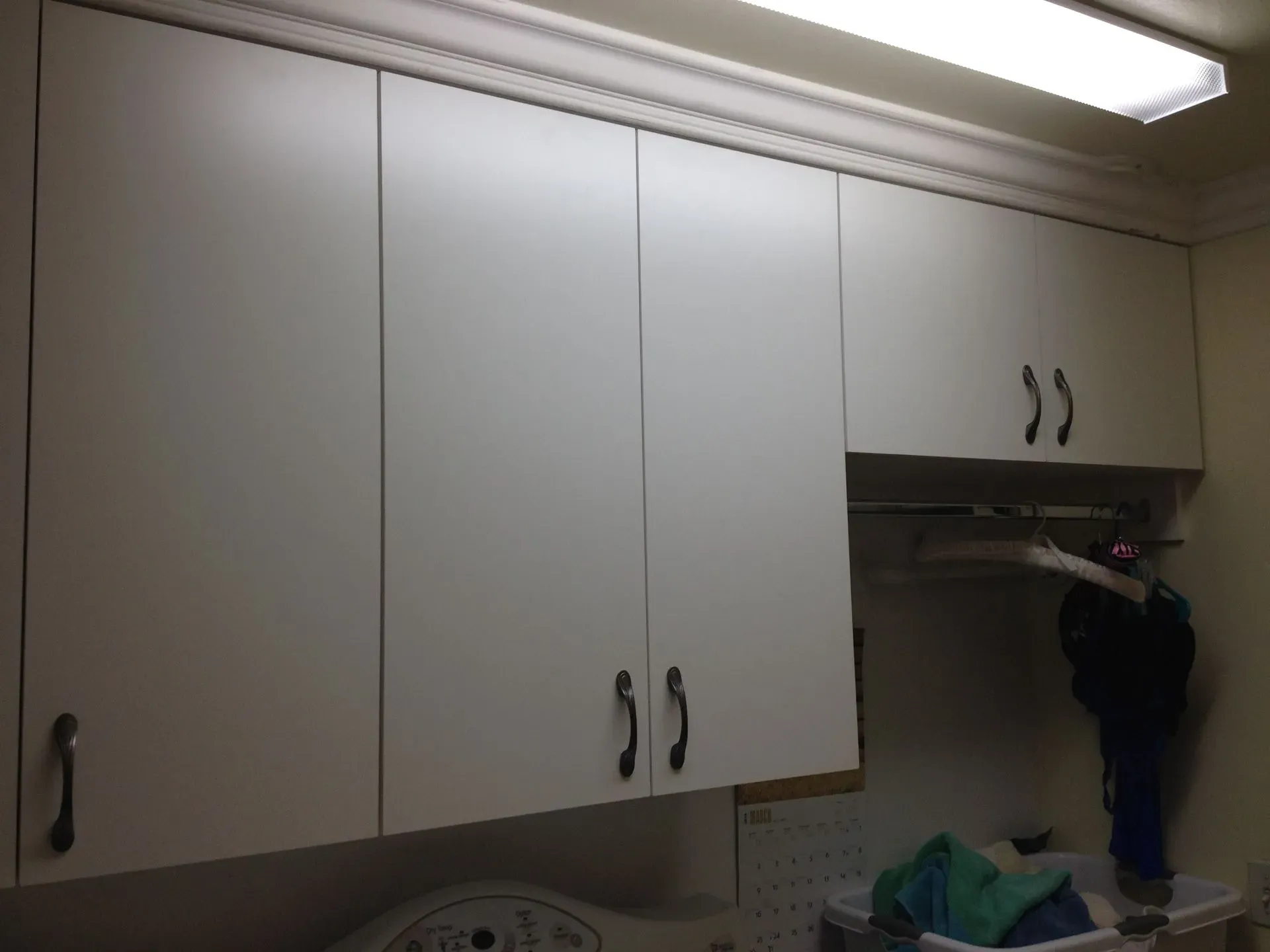 Kitchen cabinets with white doors and dark handles under a fluorescent ceiling light.