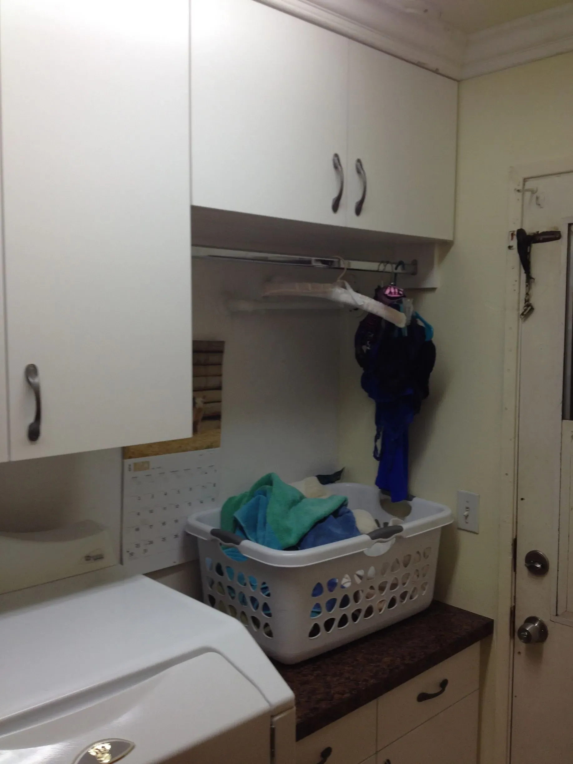 Laundry room with white cabinets, a dryer, and a laundry basket on a countertop.