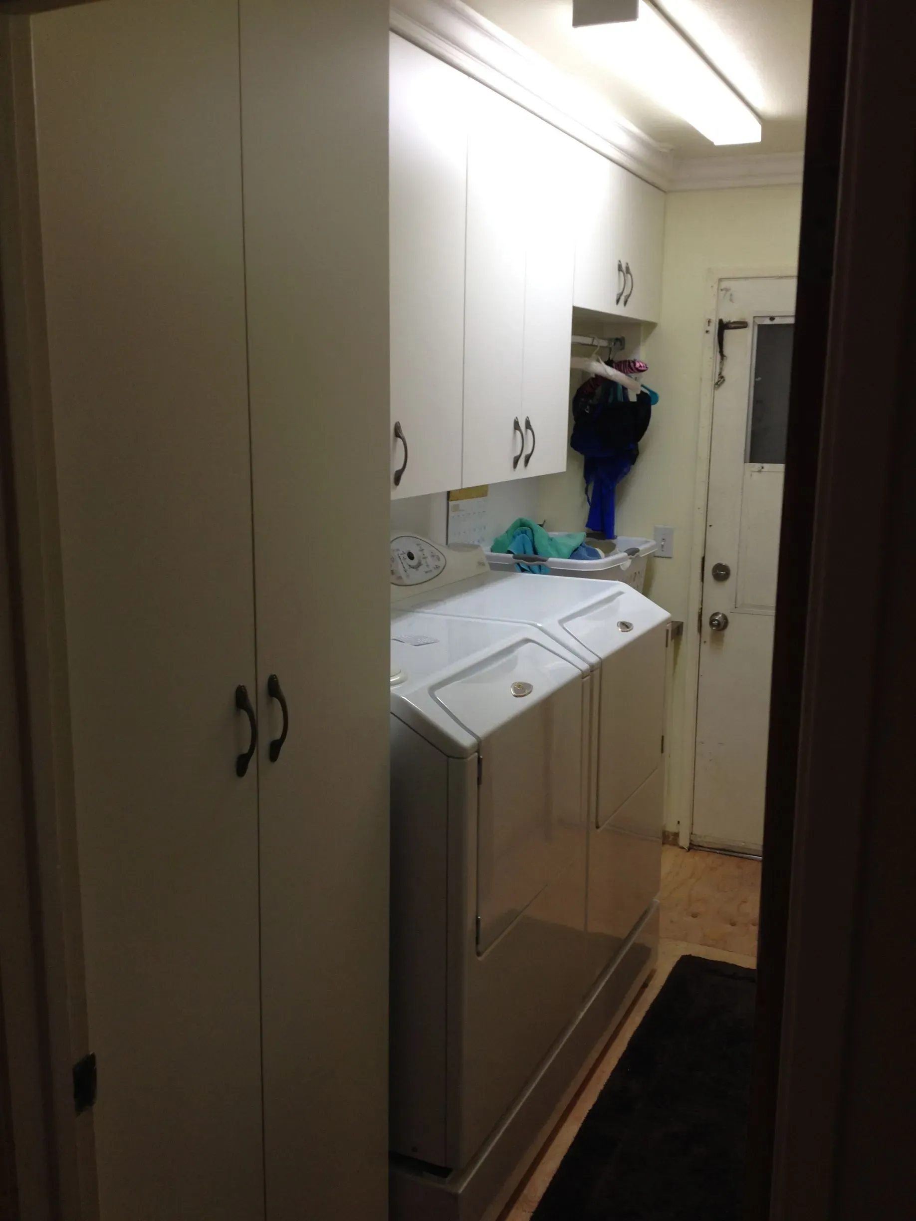 Narrow laundry hallway with white cabinets, washer and dryer, and a black runner rug