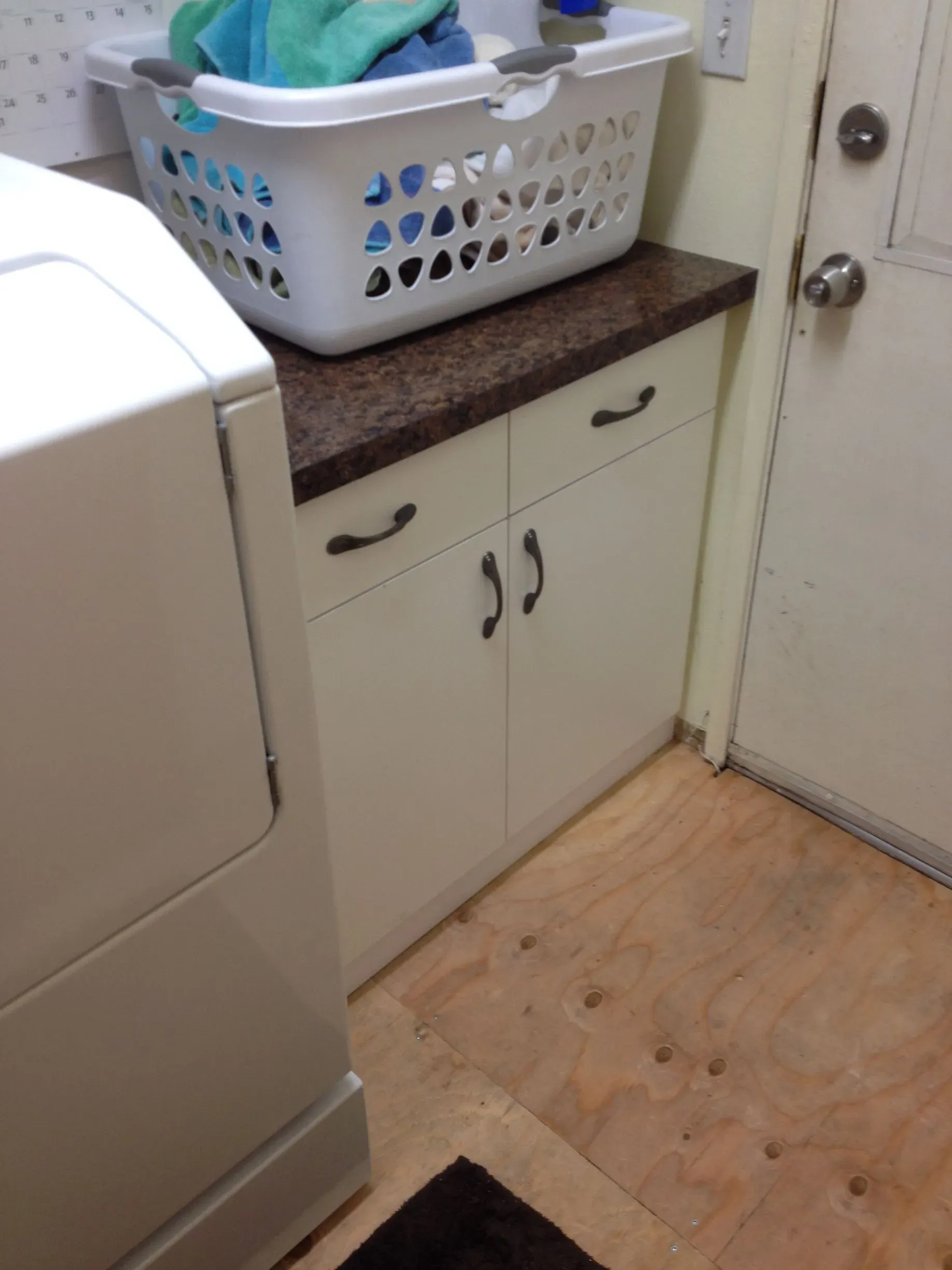 Laundry room corner with a dryer, cabinet, countertop, and laundry basket by a door.