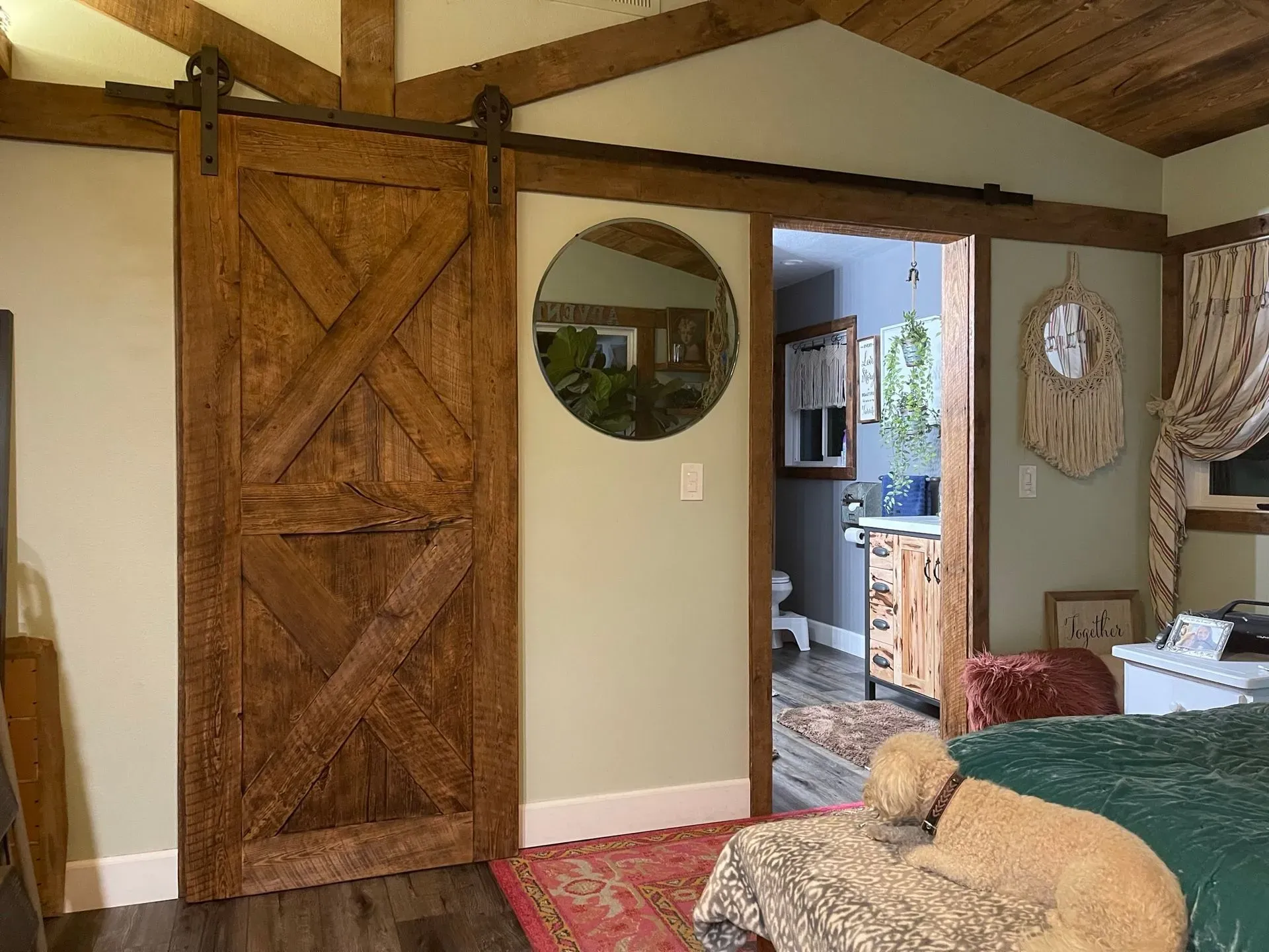 Rustic bedroom with barn-style sliding door, round mirror, and doorway to a bathroom and kitchen area