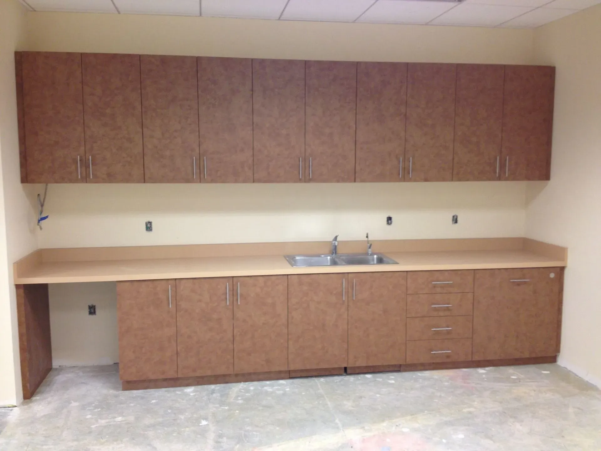 Empty room with beige cabinets and countertop, including a sink and upper storage cabinets.