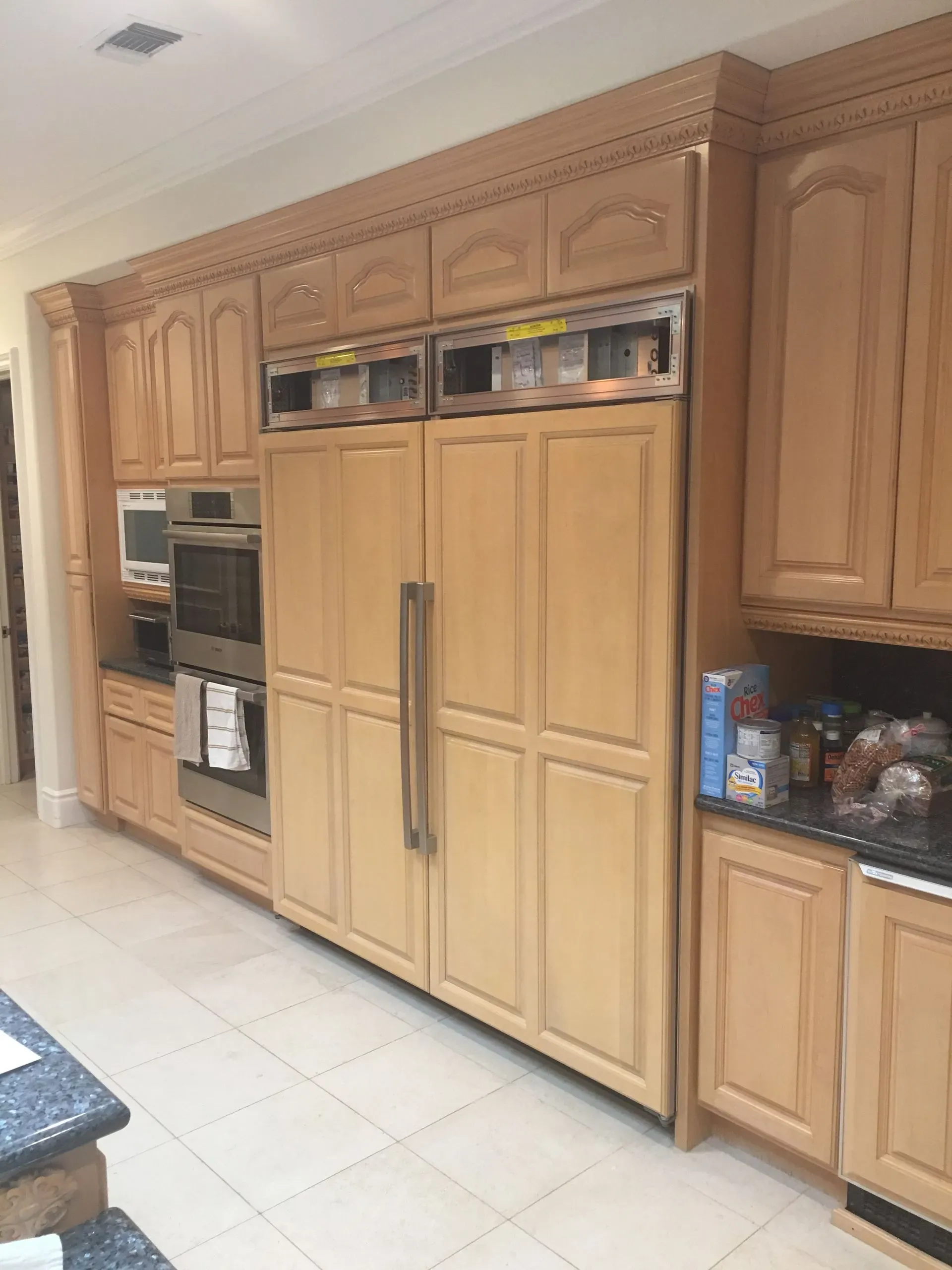 Kitchen with light wood cabinets, built-in double oven, and large stainless steel refrigerator.