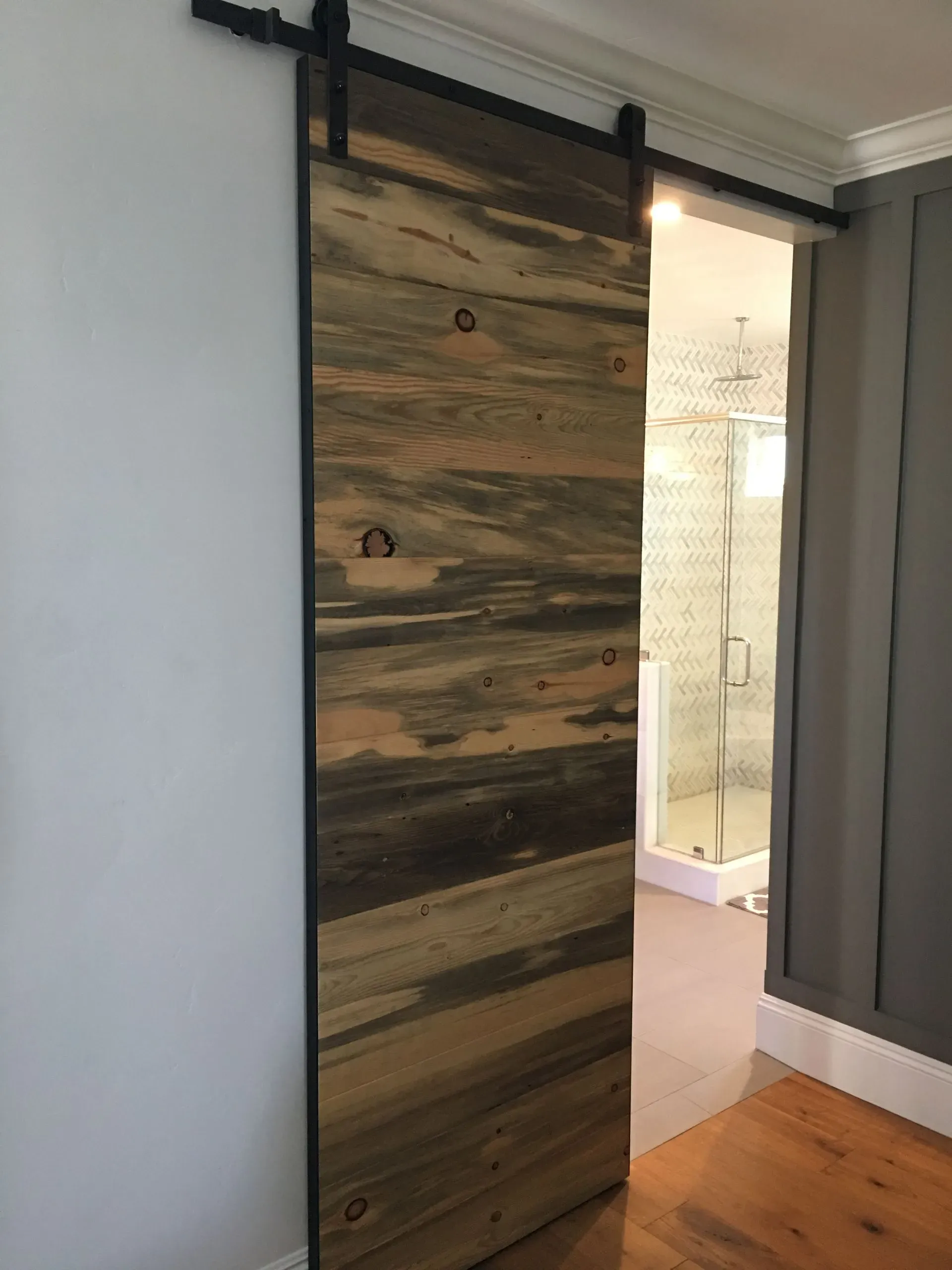 Partially open rustic wood sliding door revealing a bright bathroom interior