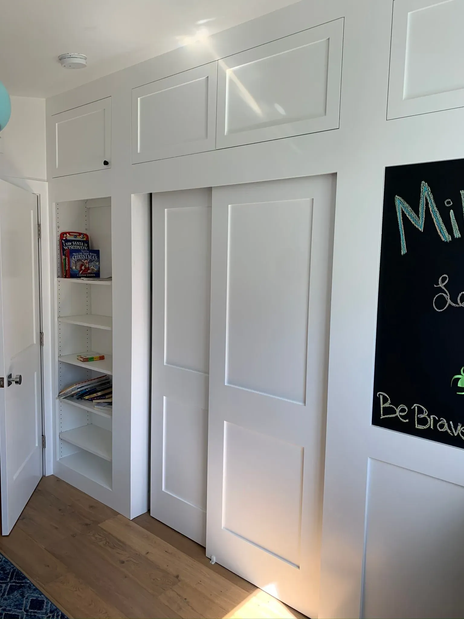 White closet doors and built-in shelves in a bright room with a black chalkboard on the wall.