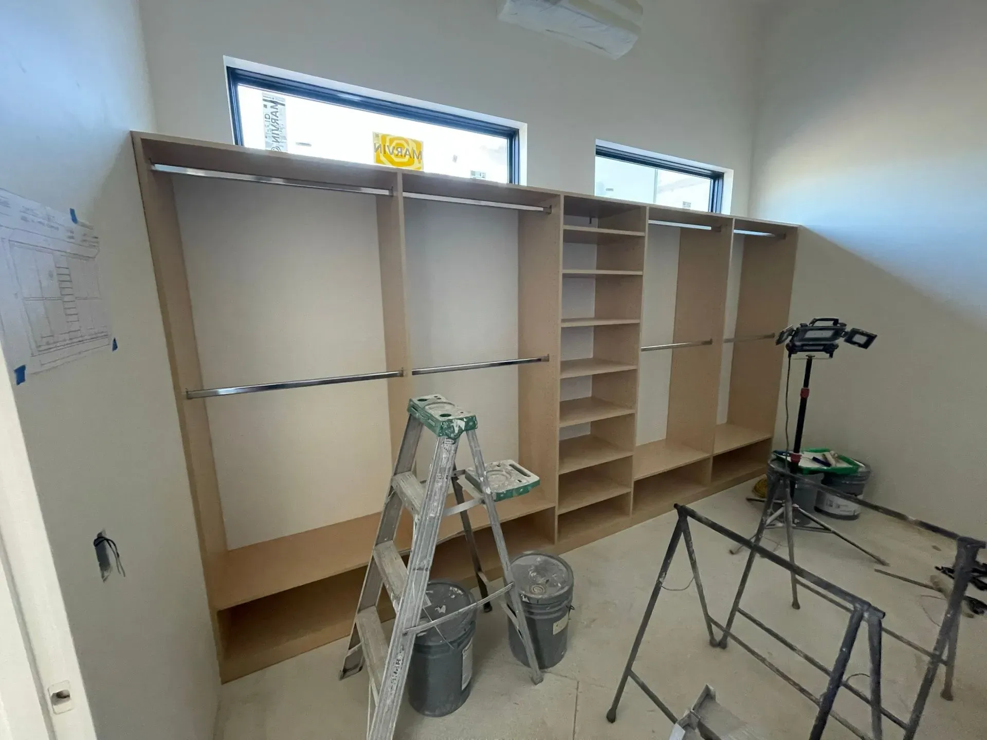 Room under renovation with built-in cabinets, ladders, and construction tools on the floor.
