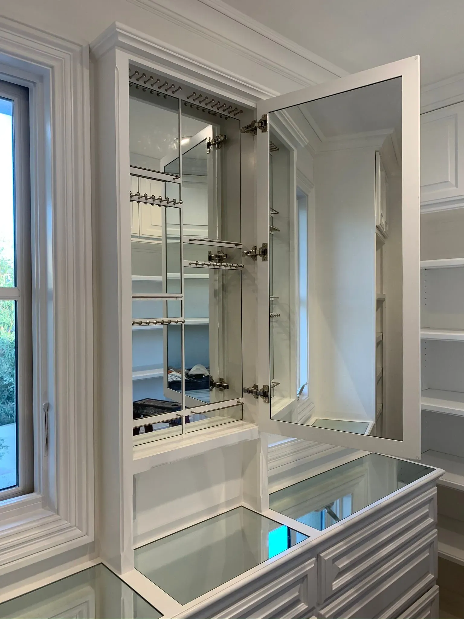 Bright bathroom vanity with an open mirrored medicine cabinet and white shelves beside a window
