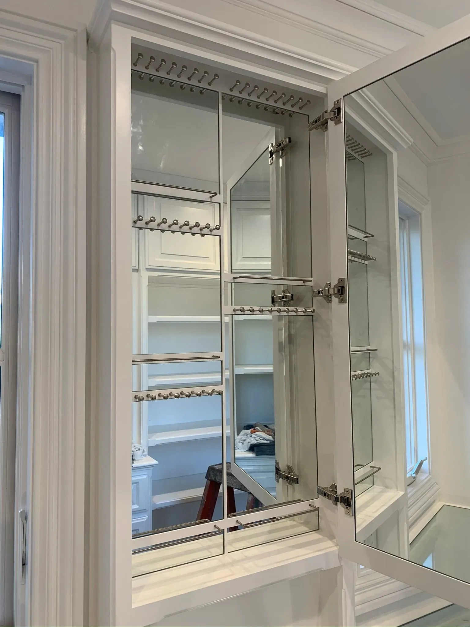 Open white window cabinet with glass panes and metal shelves in a bright room