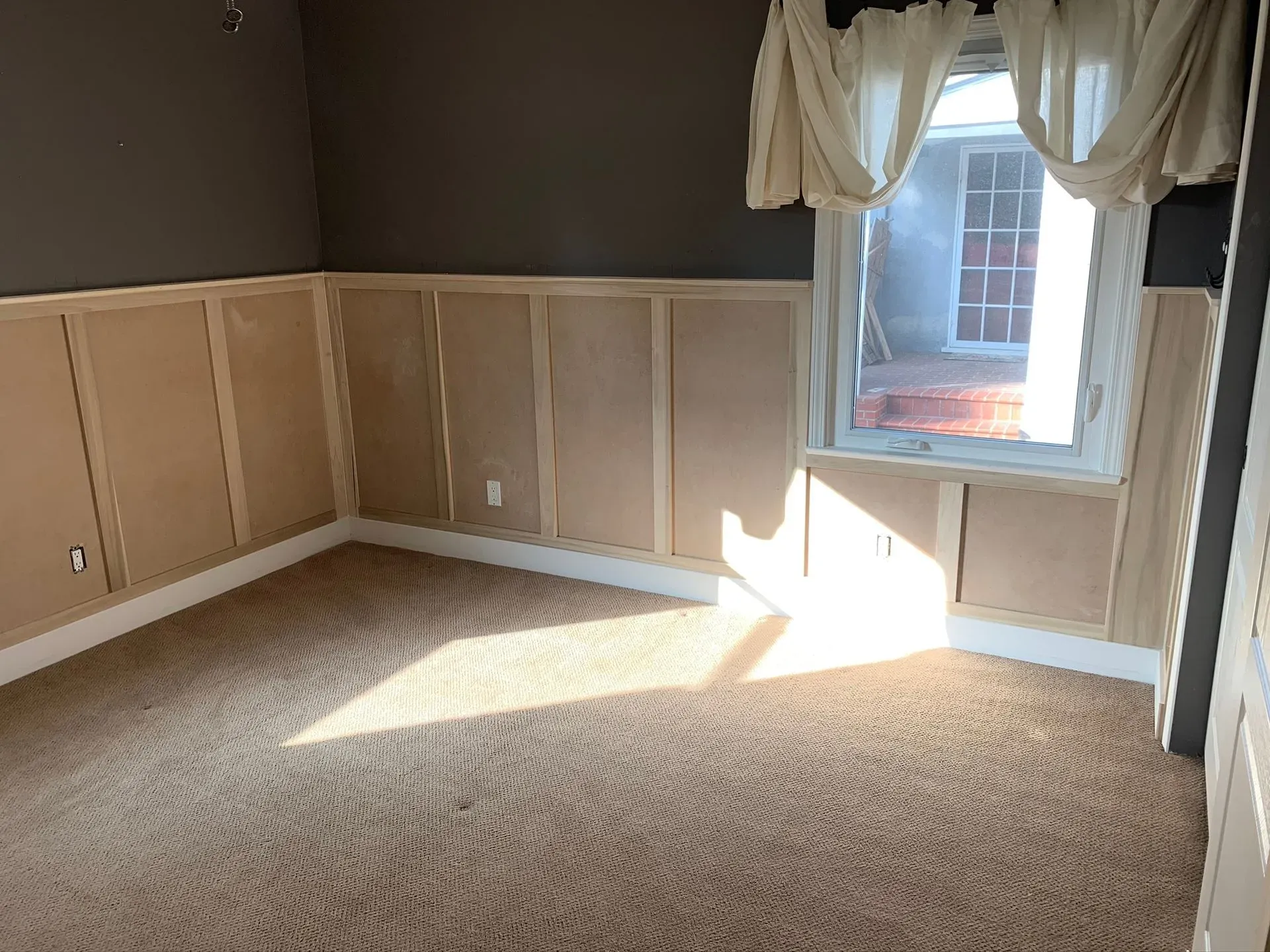 Empty carpeted room with beige wainscoting, a window, and sunlight on the floor