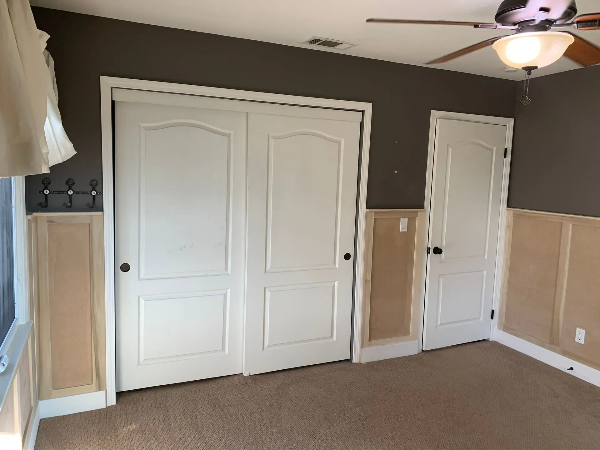 Empty bedroom with white double closet doors, a single door, beige walls, and a ceiling fan.