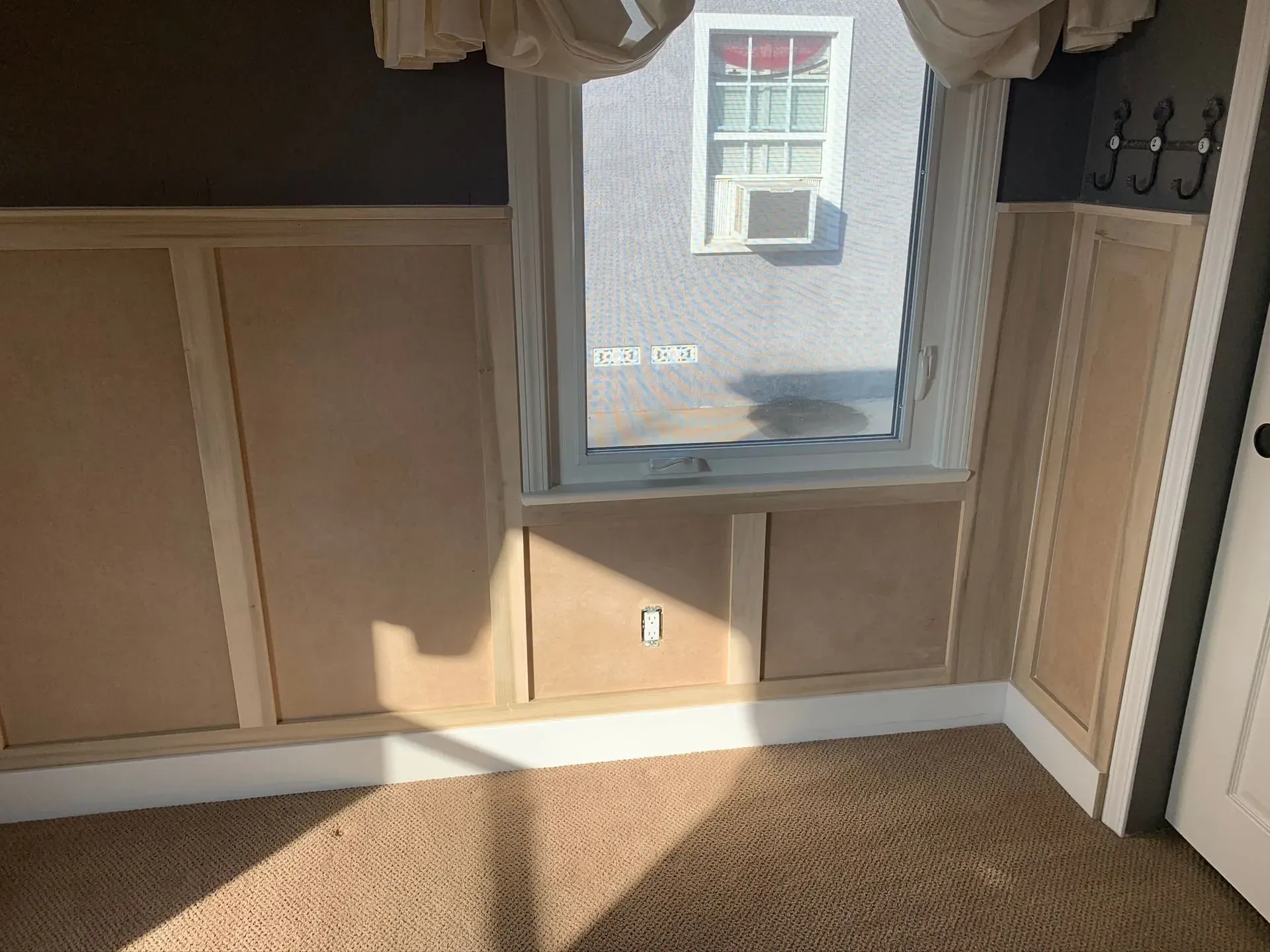Empty beige room with a window, tan carpet, and sunlight on the wall and floor.