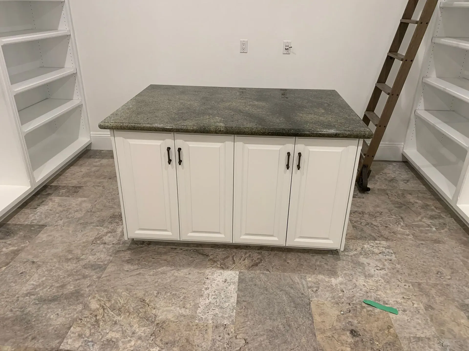 White cabinet with granite top in an empty room with built-in shelves on both sides.