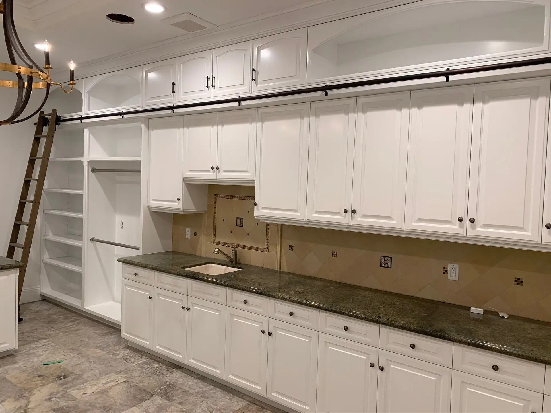 White kitchen with granite counters, built-in cabinets, and a ladder against the left wall.