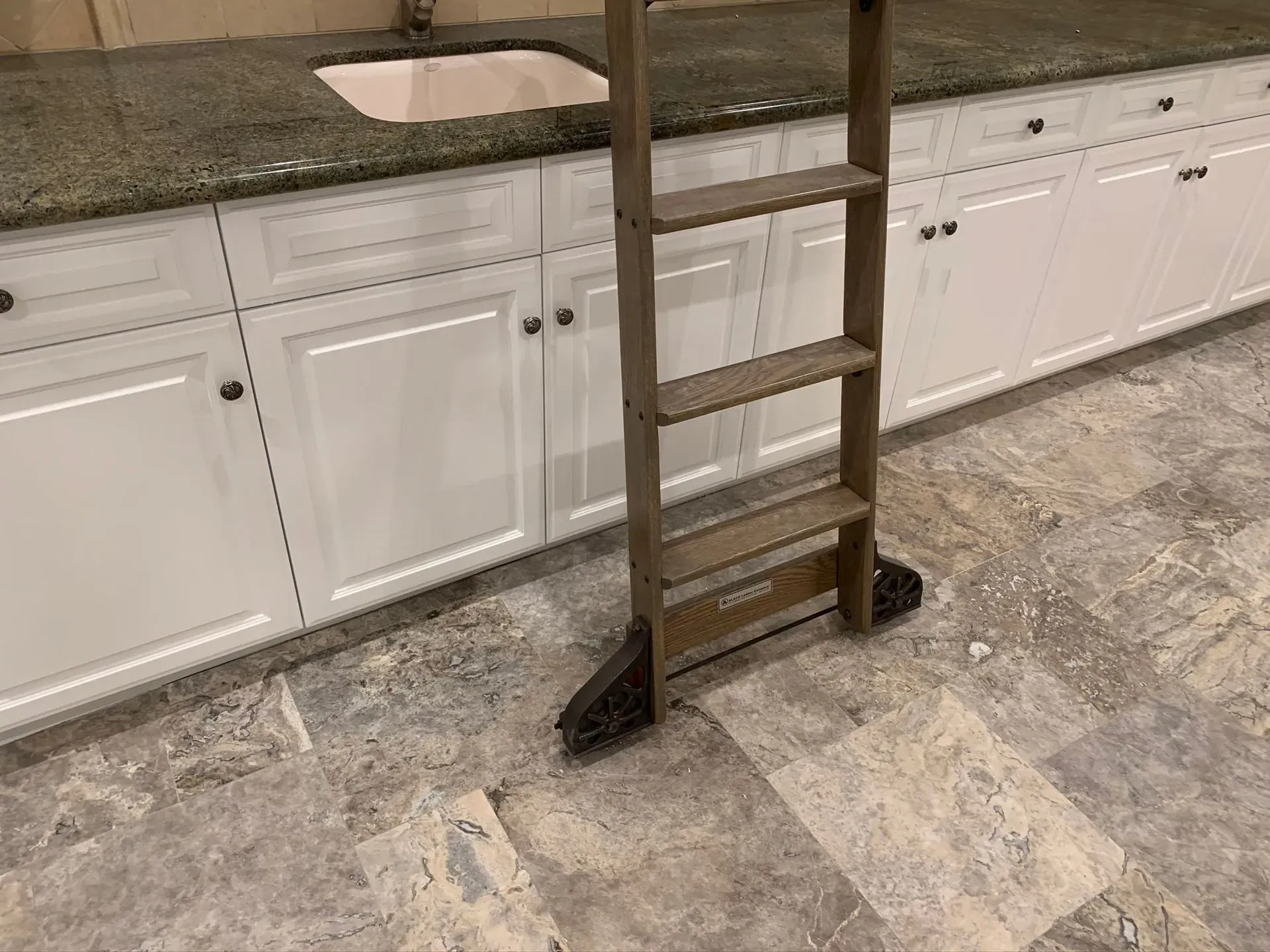 Wooden step ladder standing on a tiled kitchen floor in front of white cabinets and a countertop