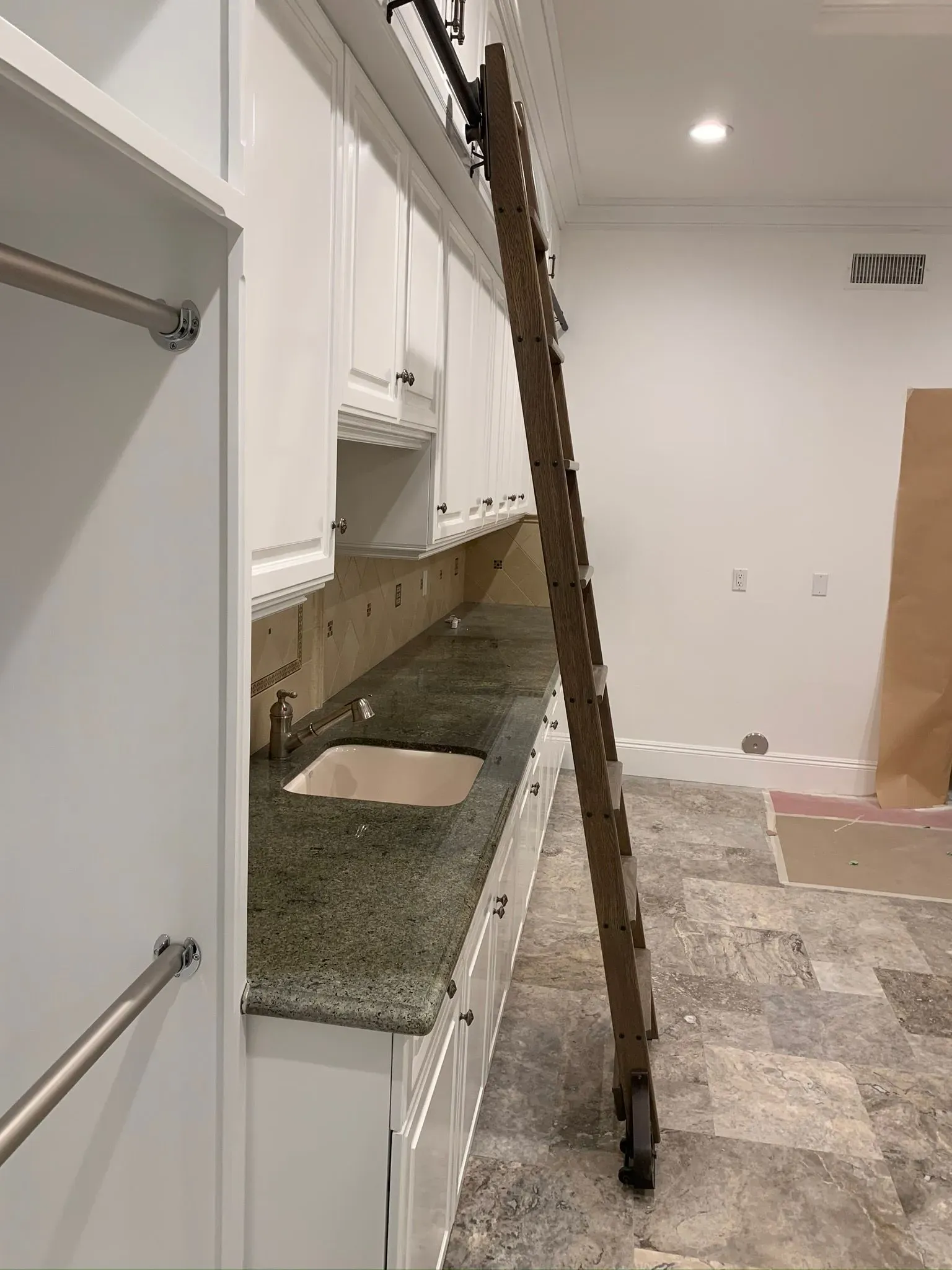 Empty kitchen under renovation with white cabinets, granite counters, and a ladder leaning across the room