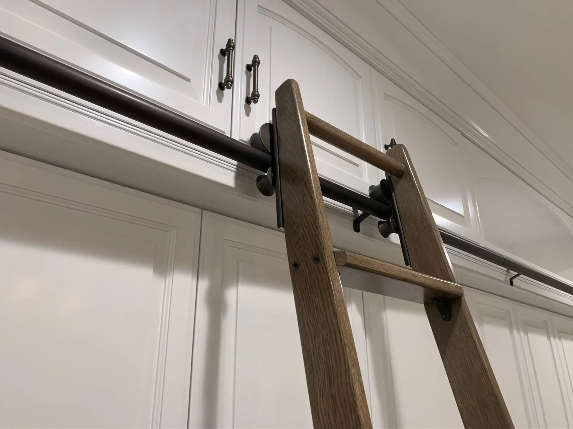 Wooden ladder leaning against a white built-in cabinet ceiling track