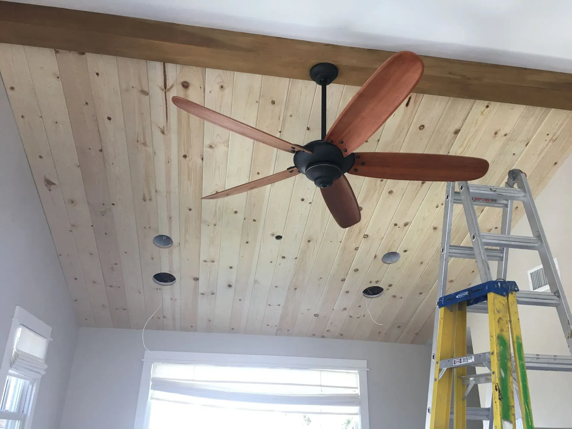 Ceiling fan on a wood-paneled ceiling with recessed lights and a ladder below