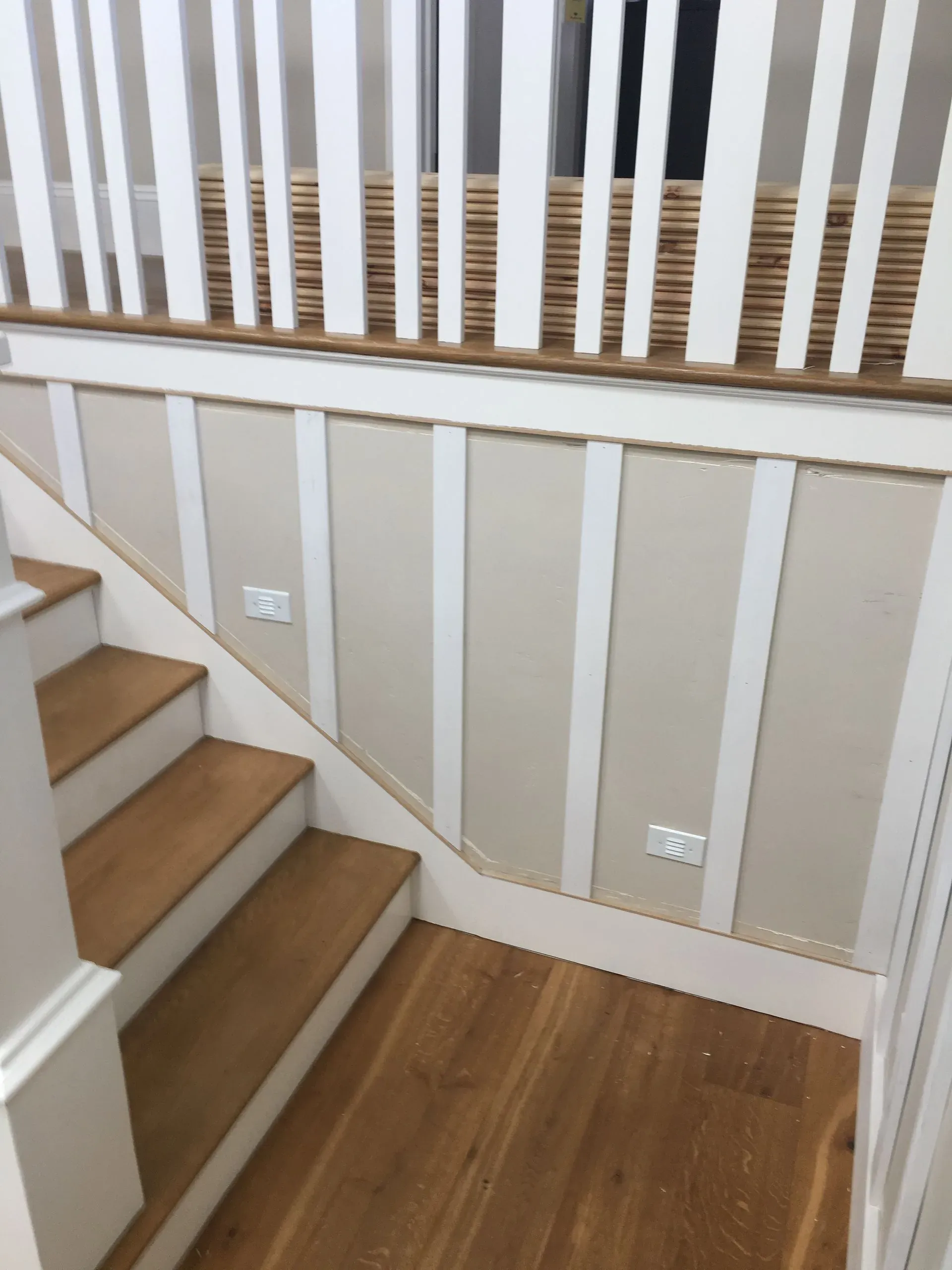 Staircase landing with white paneled walls, wood steps, and a hardwood floor.