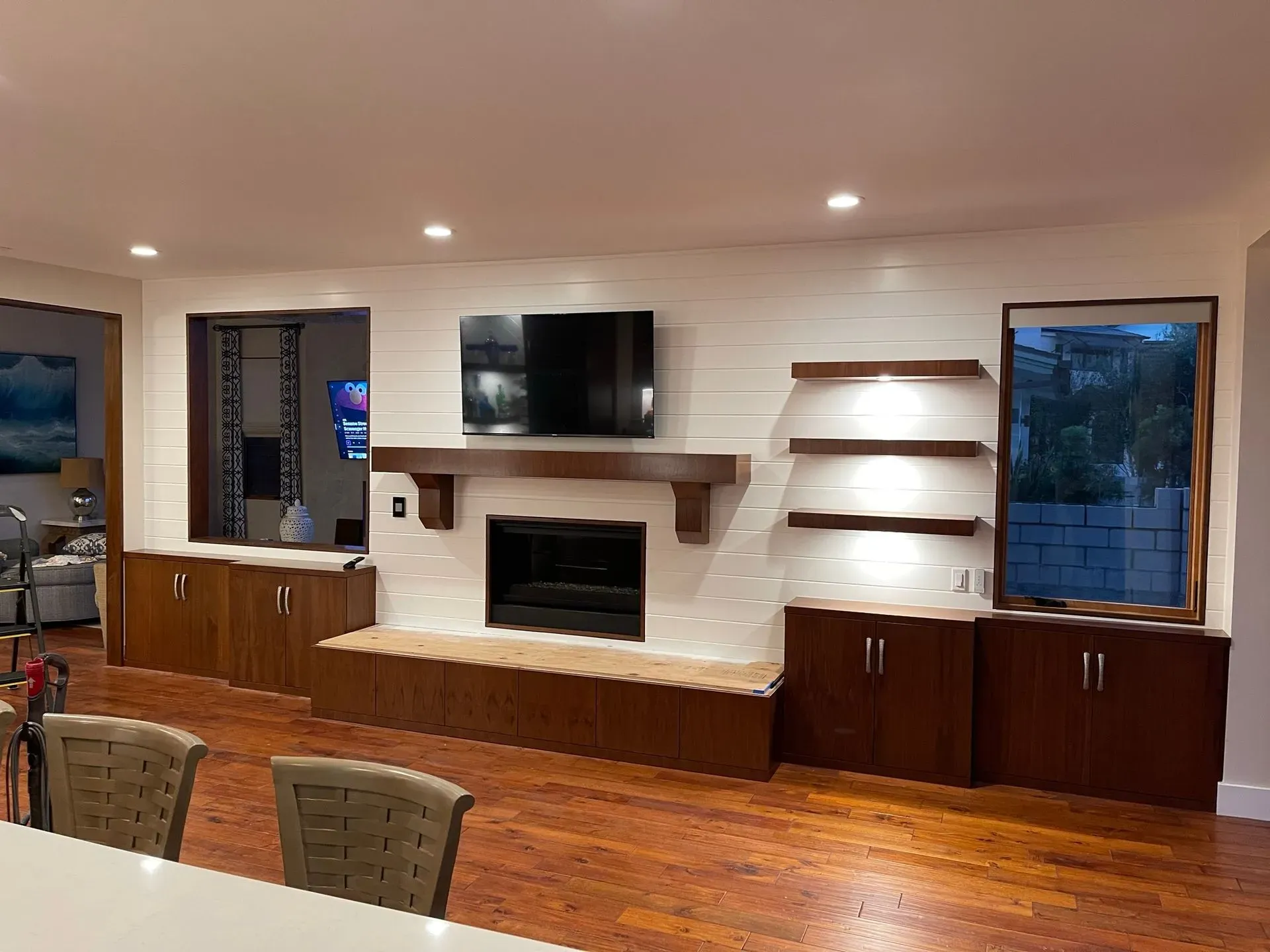 Empty living room with built-in fireplace, wall-mounted TV, wood floors, and shelves lit by recessed lights