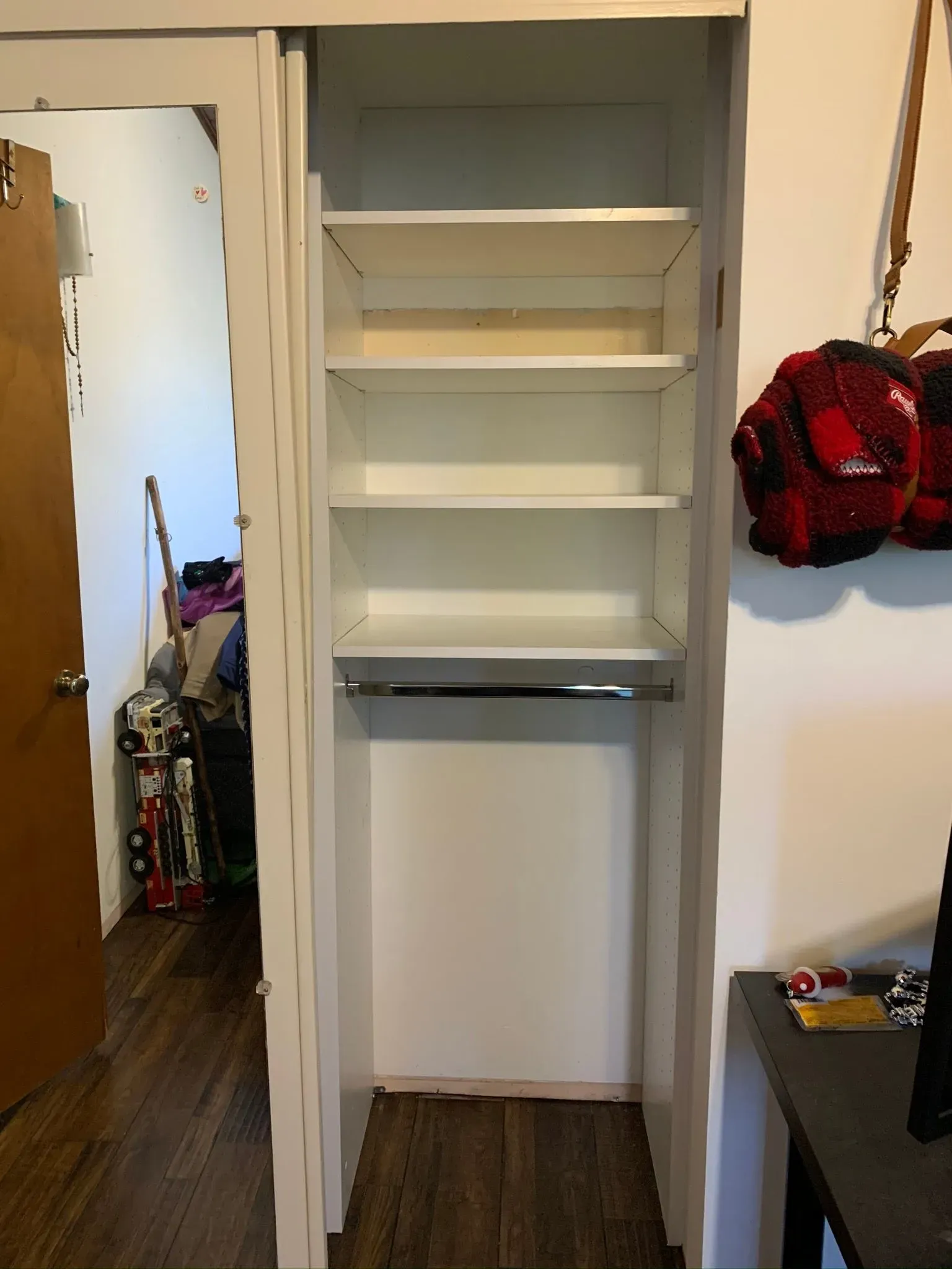 Empty closet with white shelves, hanging rod, and a doorway visible on the left; red bag hangs on the right.