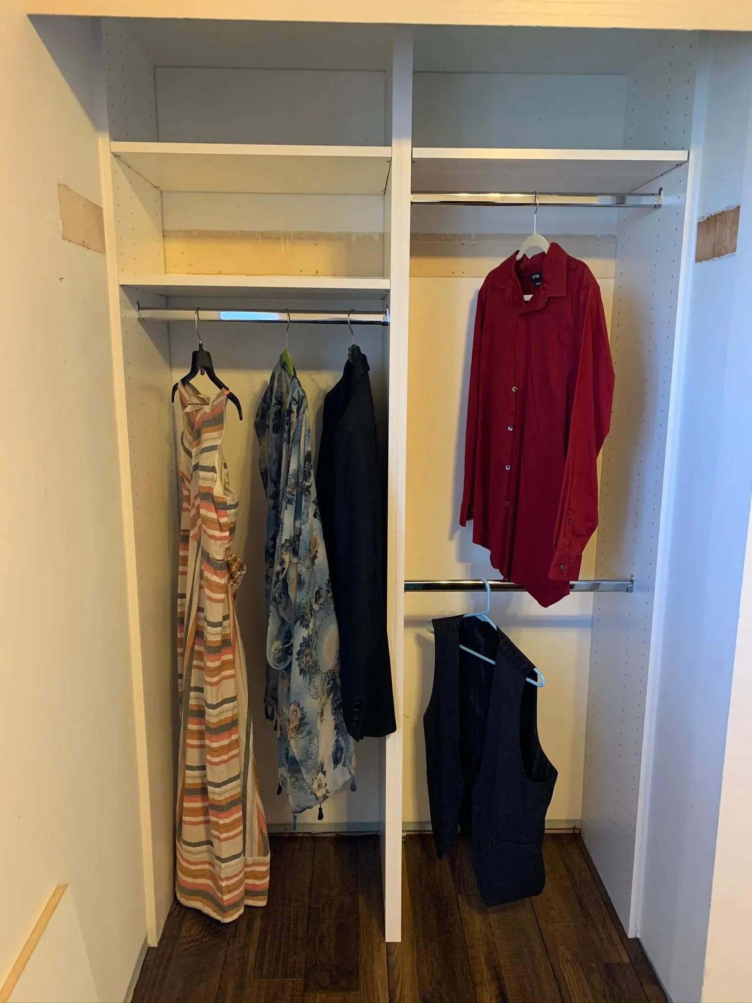 Open closet with hanging clothes, including a red shirt and patterned dresses, and a black bag on the floor.