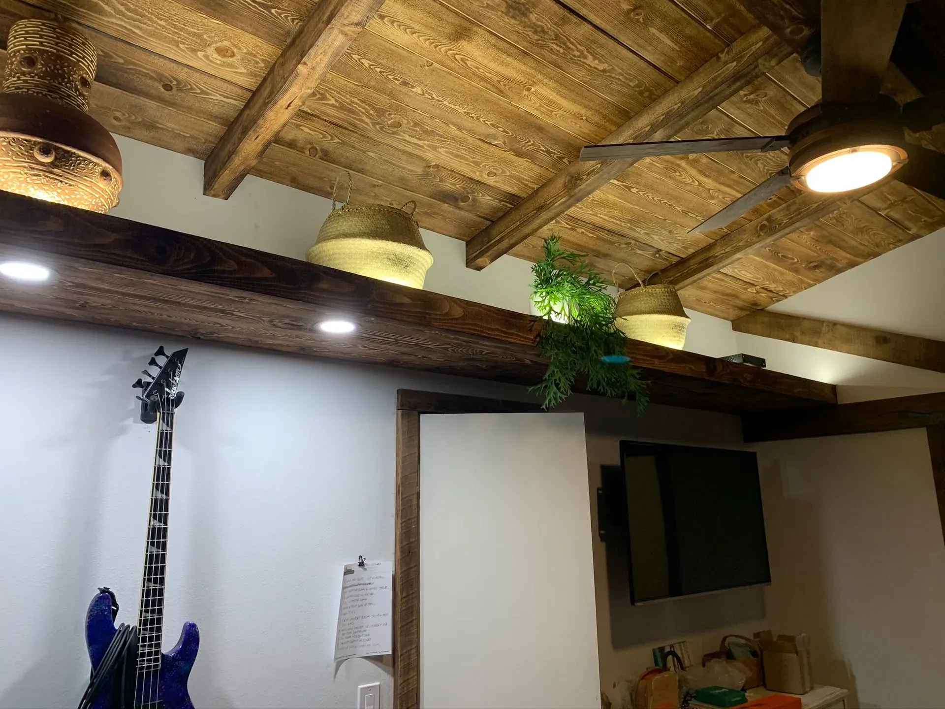 Rustic ceiling with wooden beams, round lights, and a blue guitar hanging on the wall below