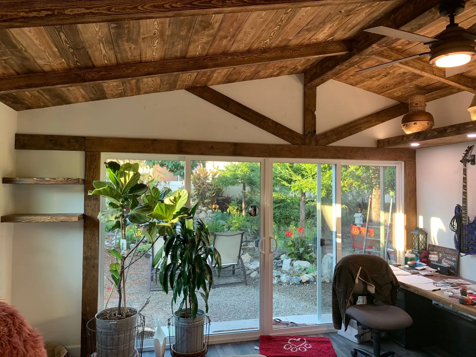Cozy room with wood-beamed ceiling, sliding glass doors, plants, and a desk by a garden view