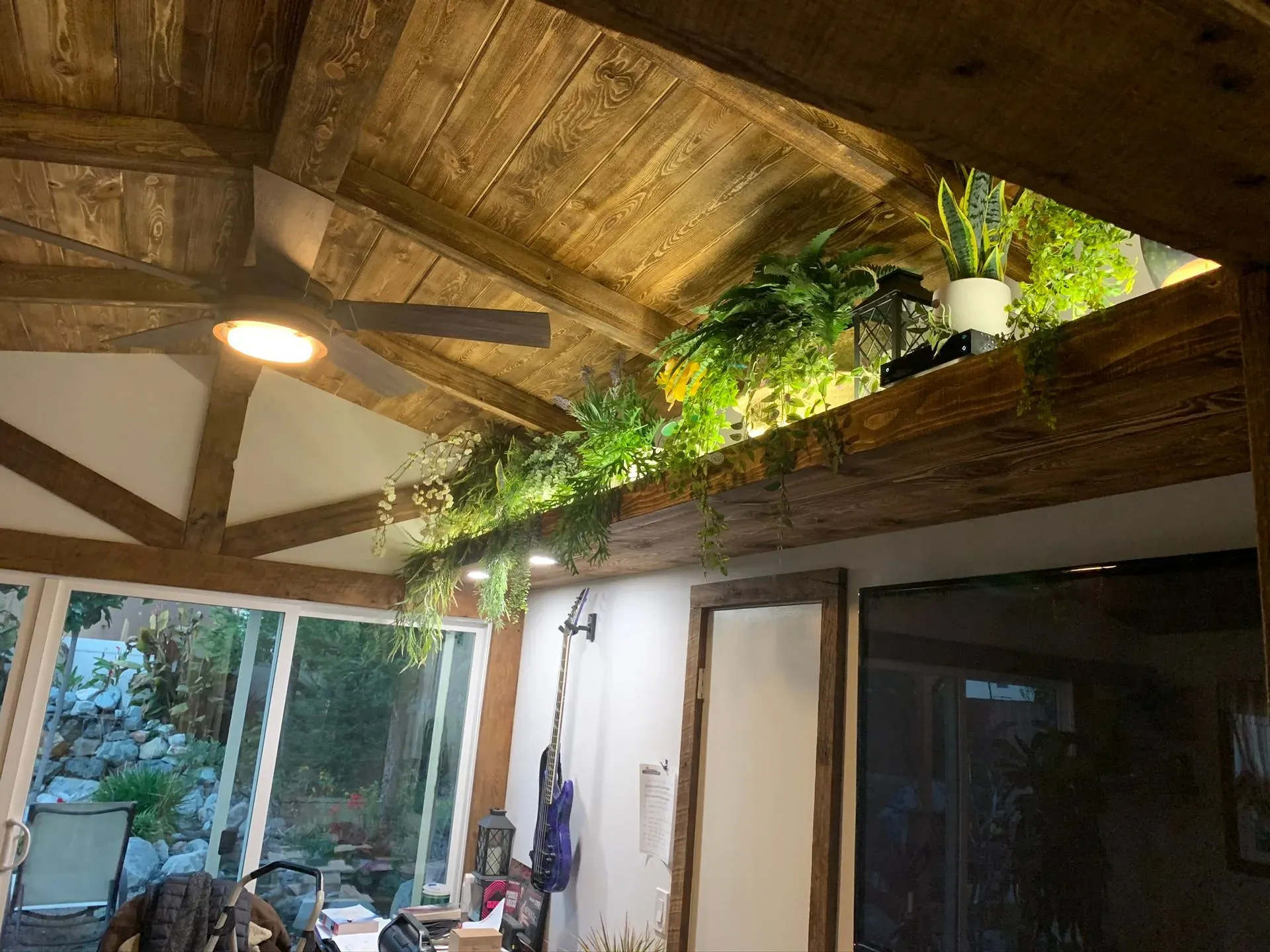 Rustic indoor patio with wooden beams, skylight plants, ceiling fan, and sliding glass doors.