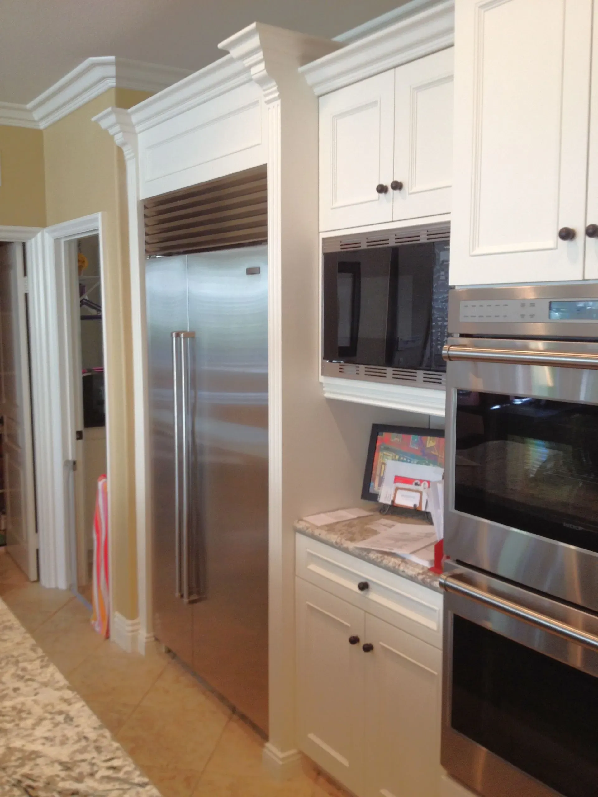 Kitchen with stainless steel refrigerator, built-in oven, and white cabinets.